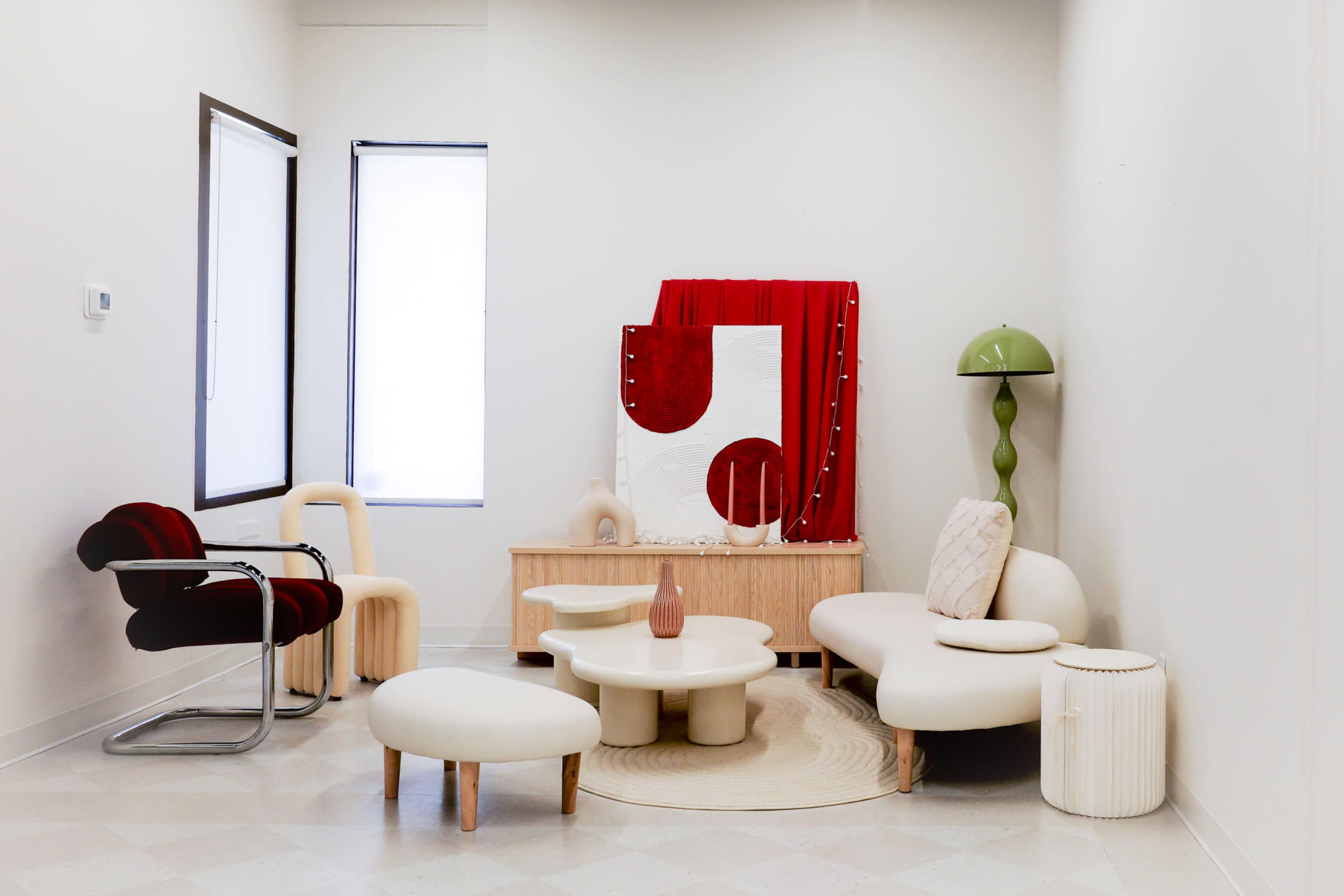 The room features modern furniture, including a red chair, a white sofa, a round coffee table, and a cabinet, with decorative elements like a tall green lamp and a large red backdrop.