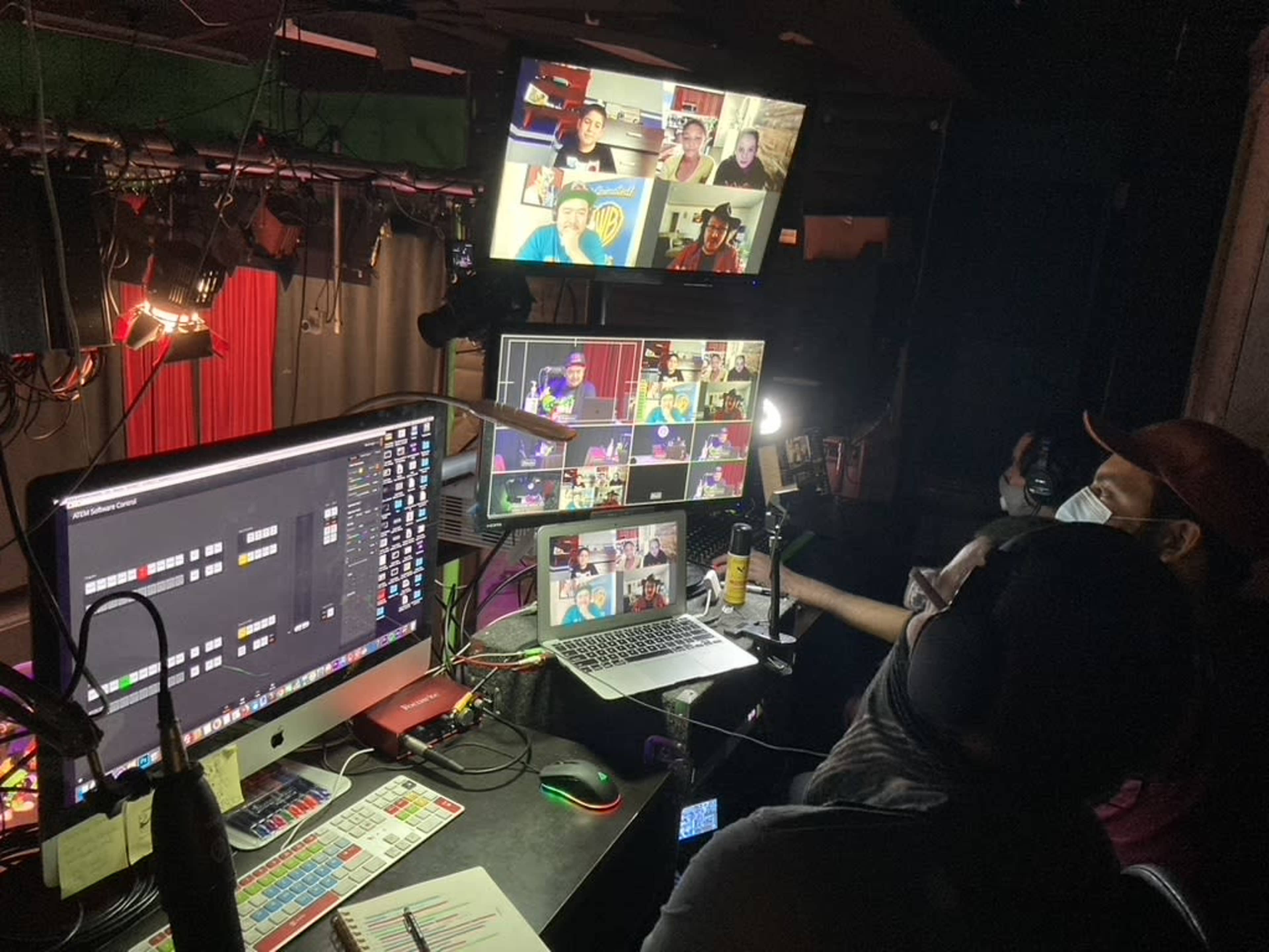 A control room filled with monitors displays multiple video feeds from a virtual event, while a person works at a desk surrounded by audio and video equipment.