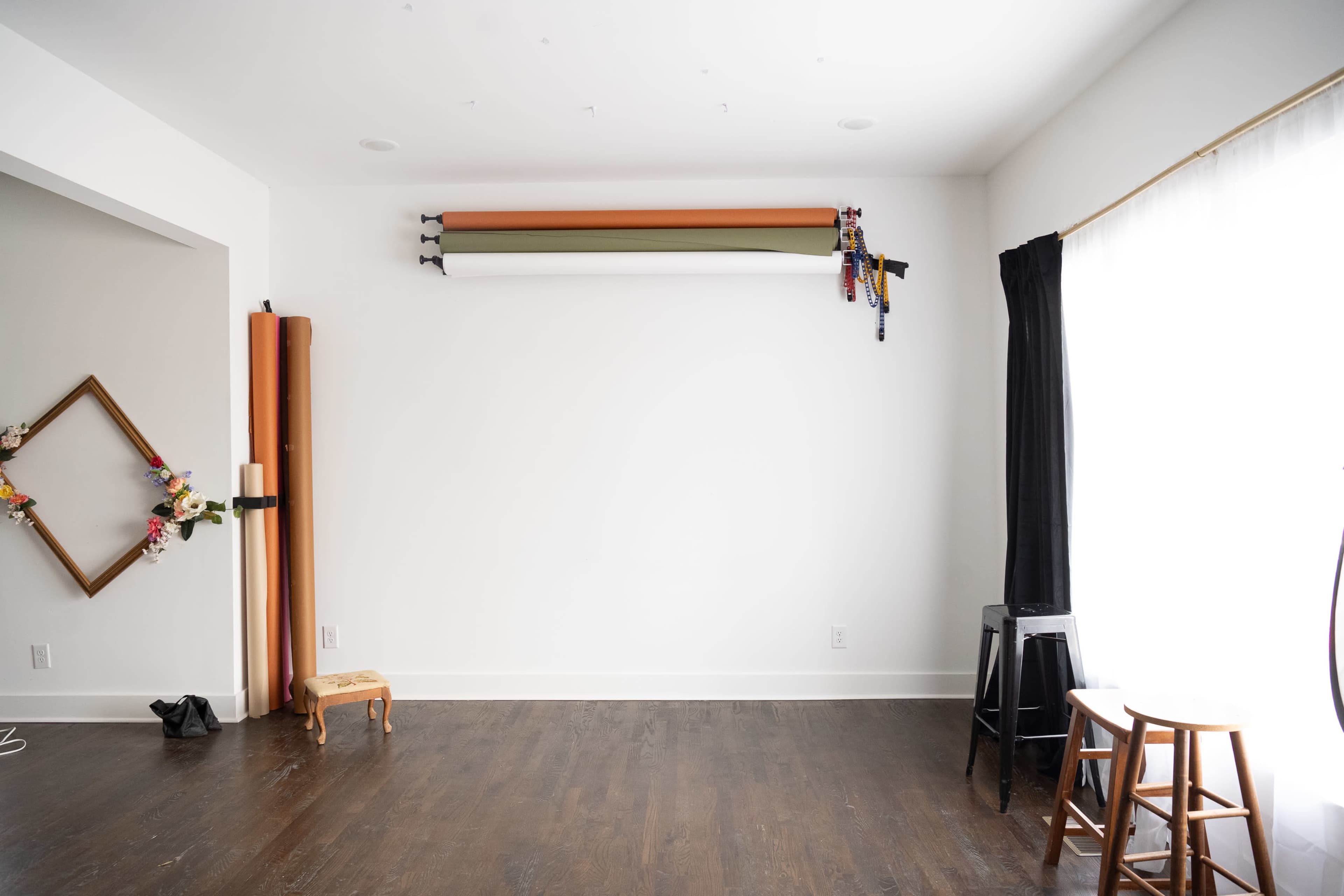 A minimalistic studio space with a white wall, two stools, and rolls of background paper mounted above.
