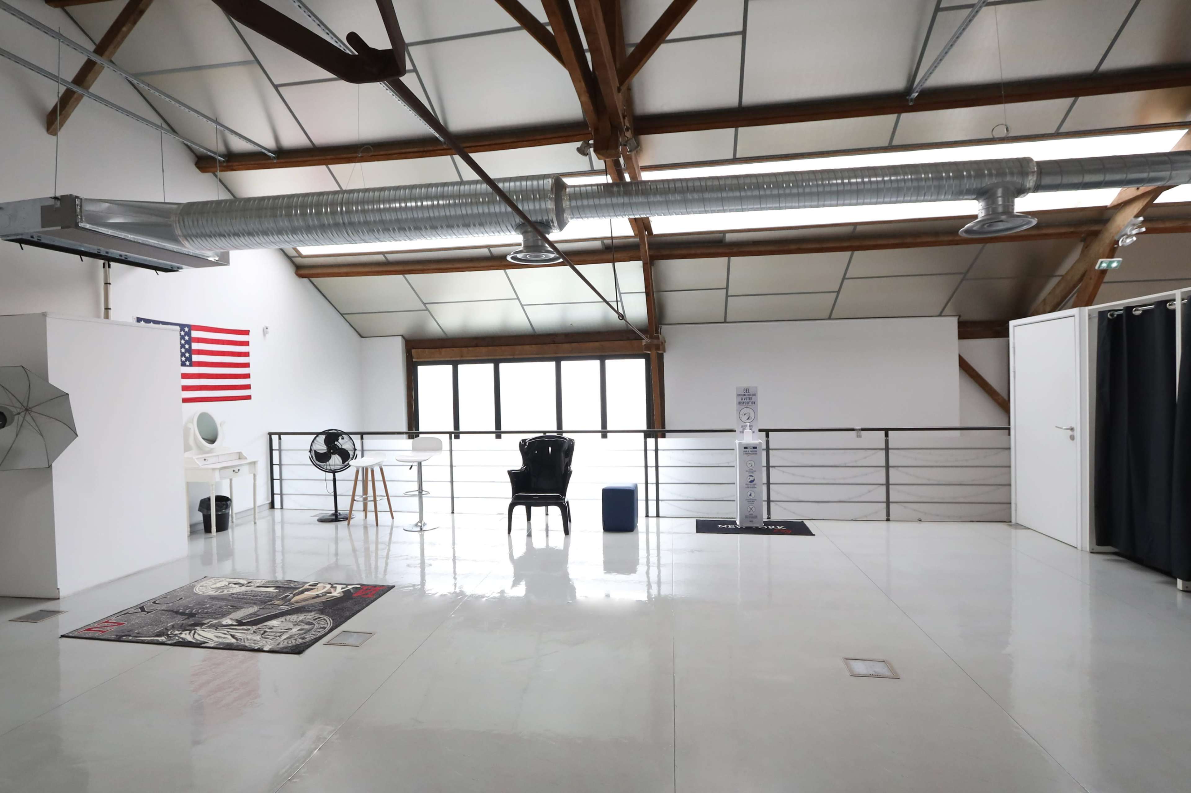 A spacious, airy room with high ceilings, featuring an American flag, various furnishings, and large windows.