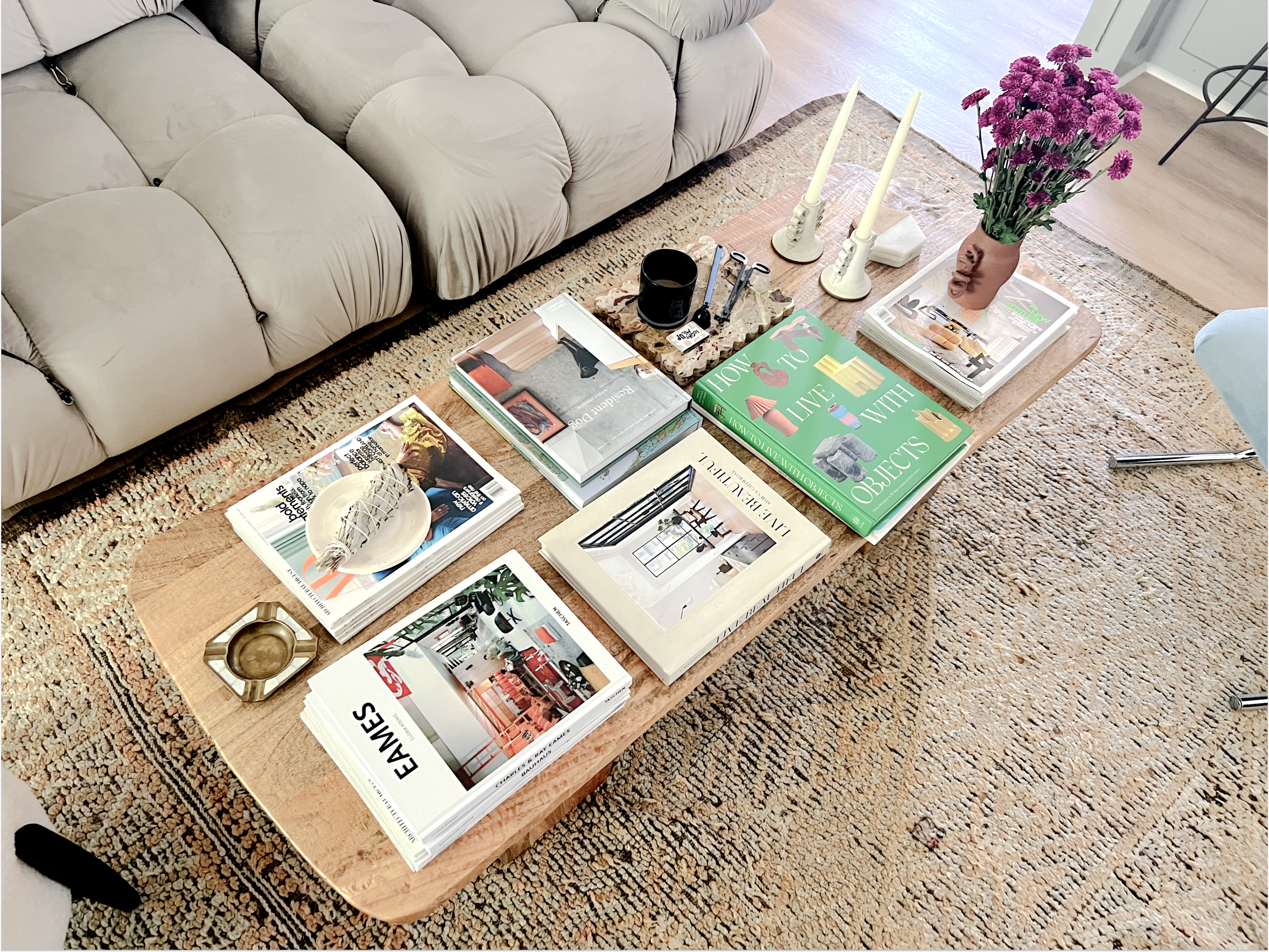 A coffee table displays various books, a candlestick, a small vase of flowers, and decorative items on a textured rug.