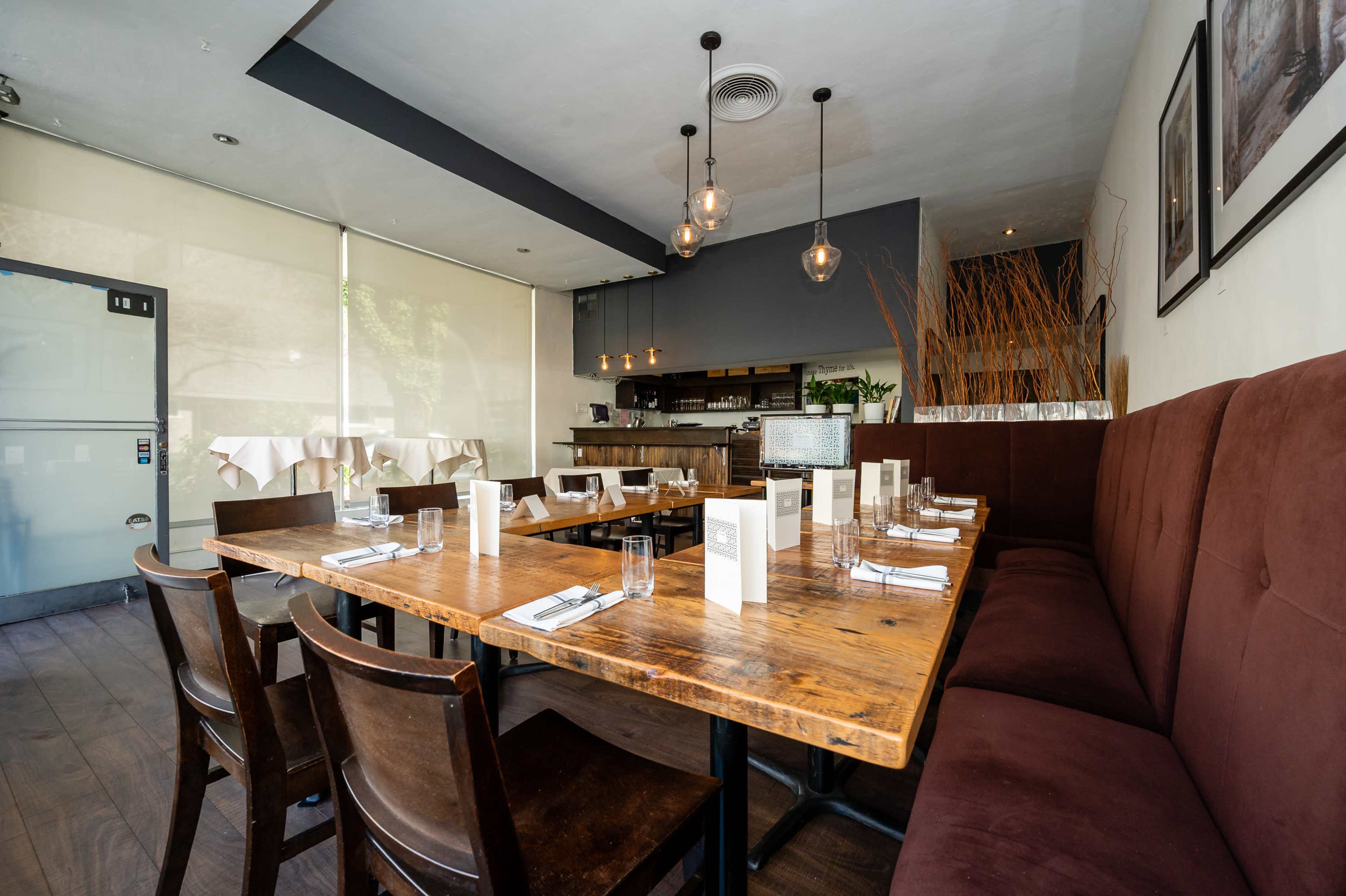 A restaurant interior featuring wooden tables set with menus and glassware, surrounded by brown upholstered seating along the wall.