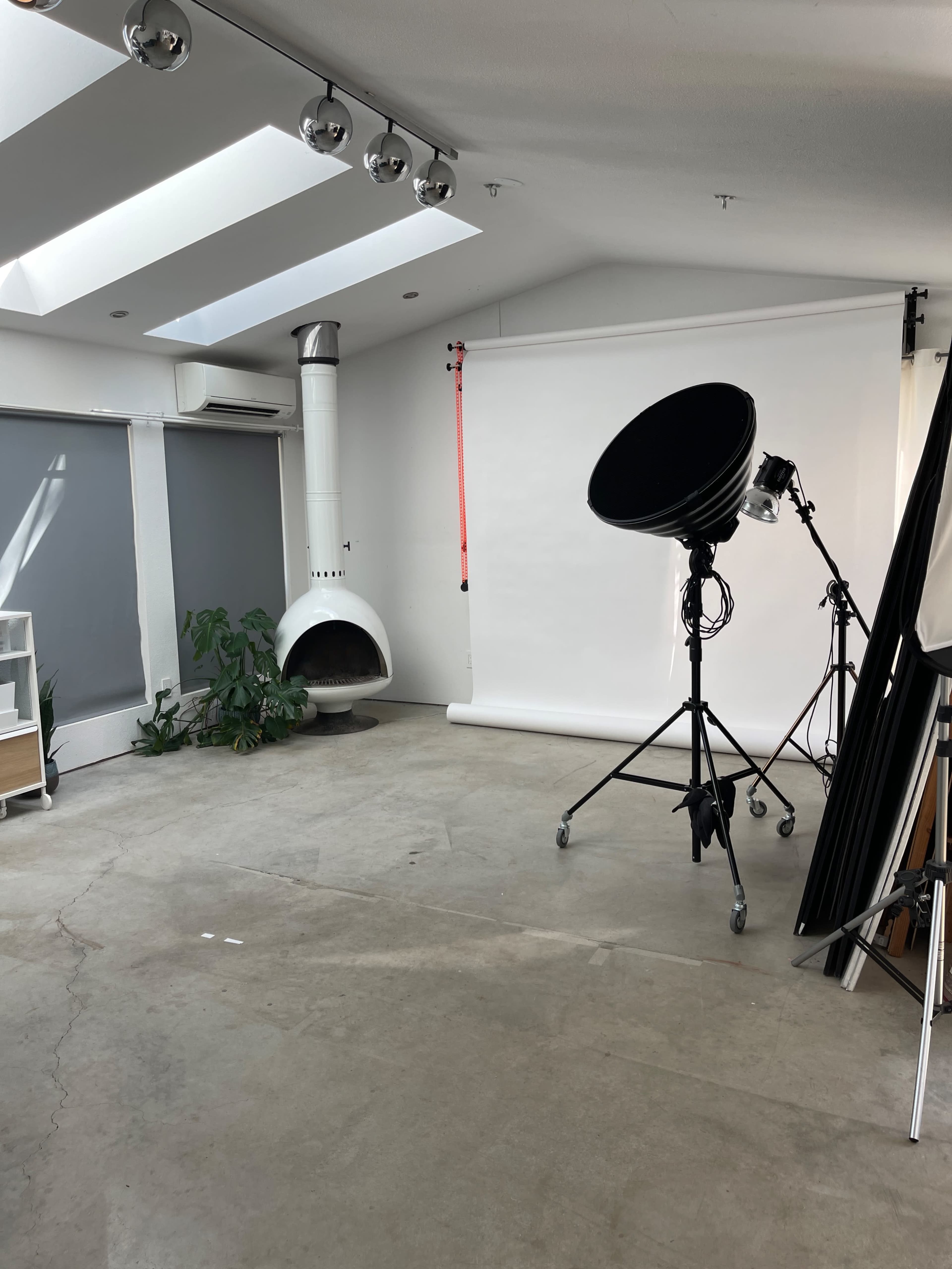 The image shows a photography studio with a white backdrop, a large softbox light on a stand, a comfortable seating area, and a modern fireplace.