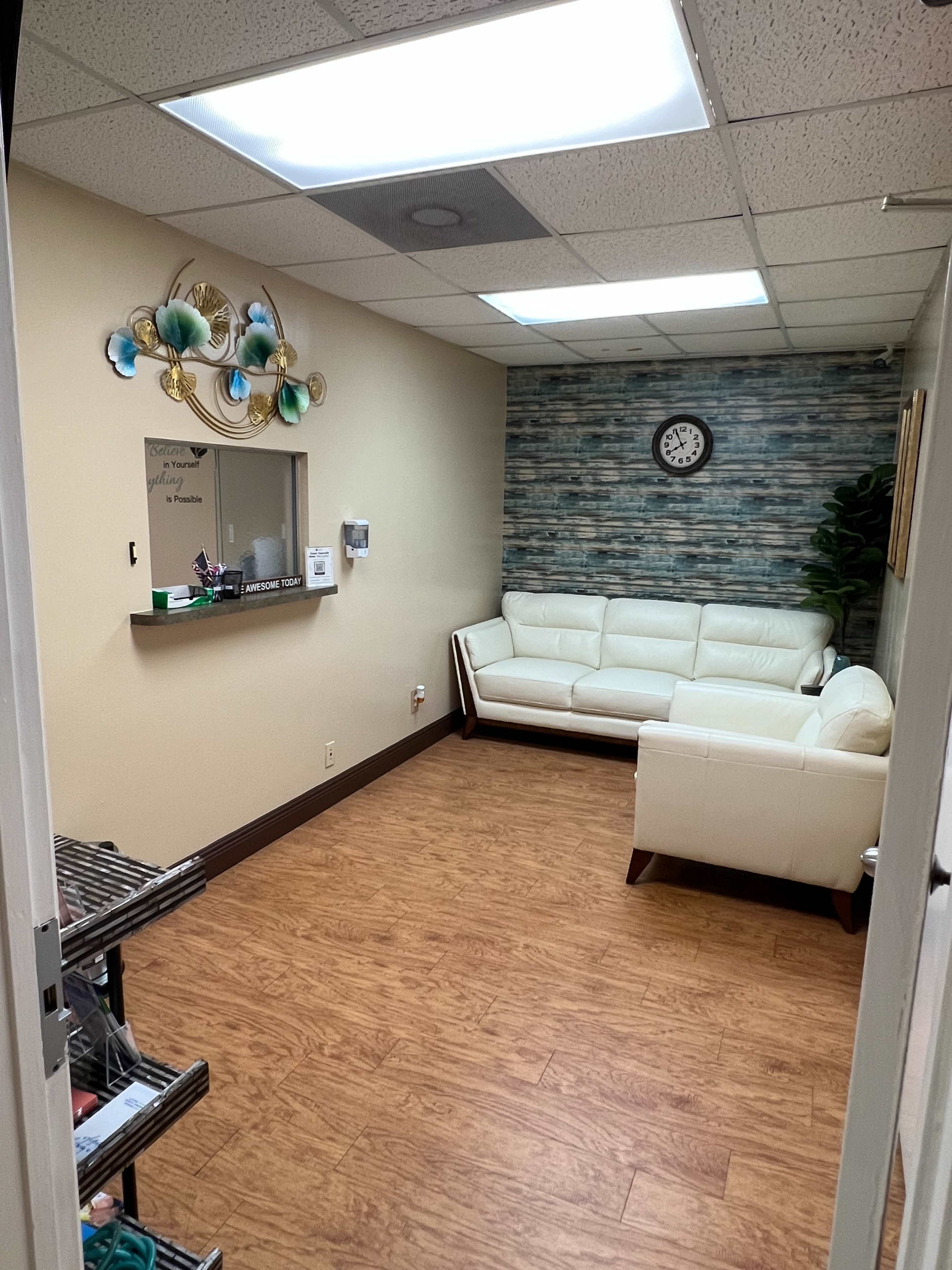 A waiting room with a white leather sofa, a wall clock, and a decorative wall featuring wooden panels.