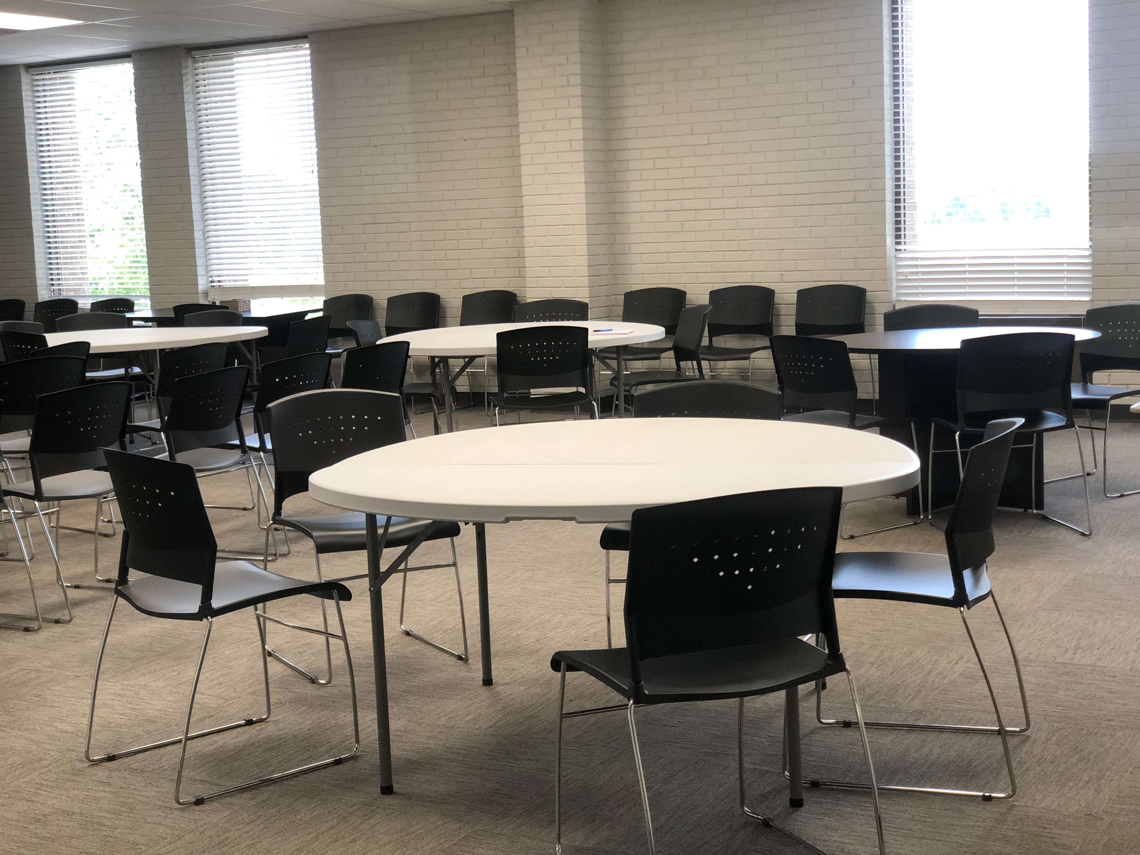 A spacious room filled with round tables and black chairs arranged in a grid formation.