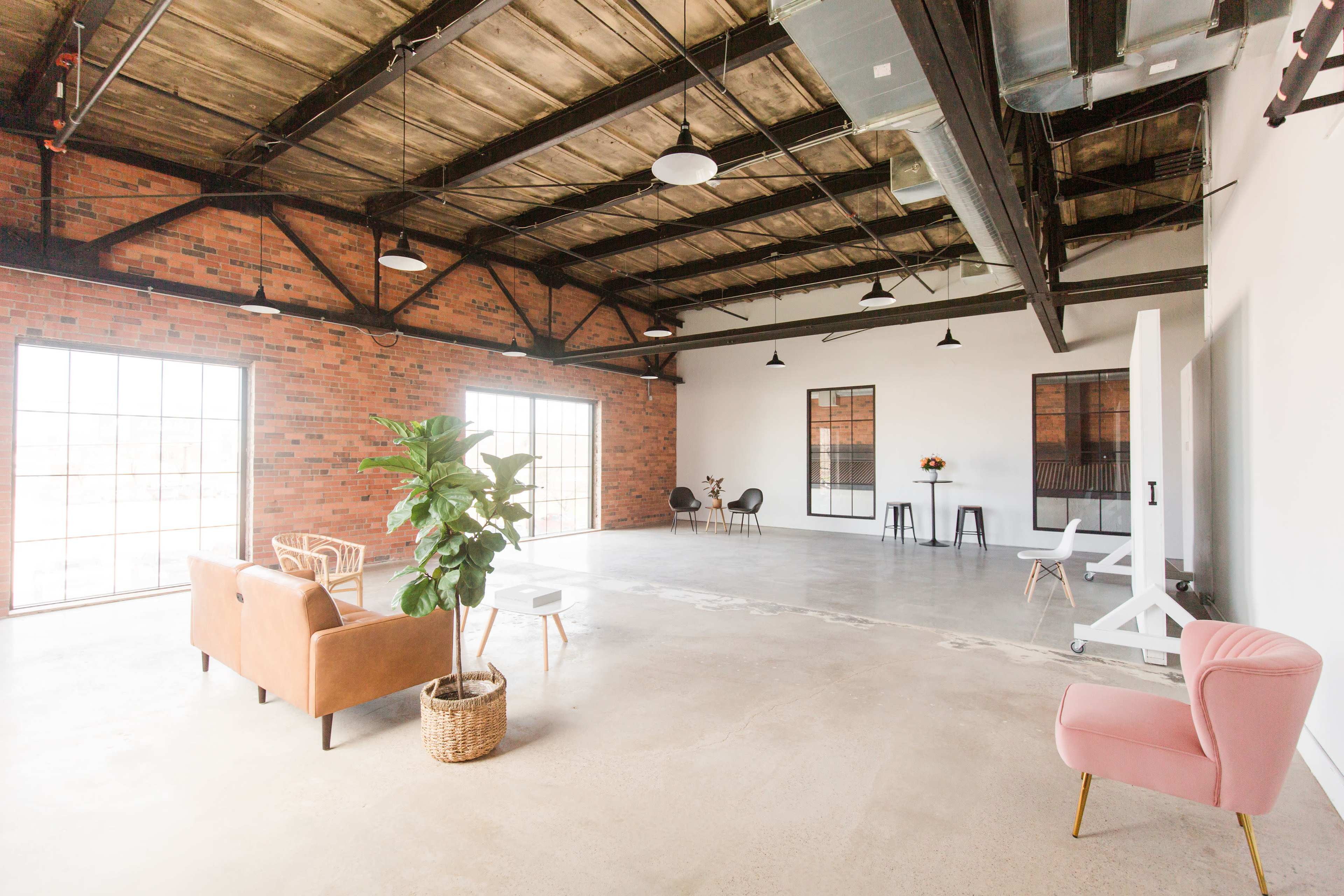 A spacious, modern interior with exposed brick walls, large windows, and minimalistic furniture, including two seating areas.