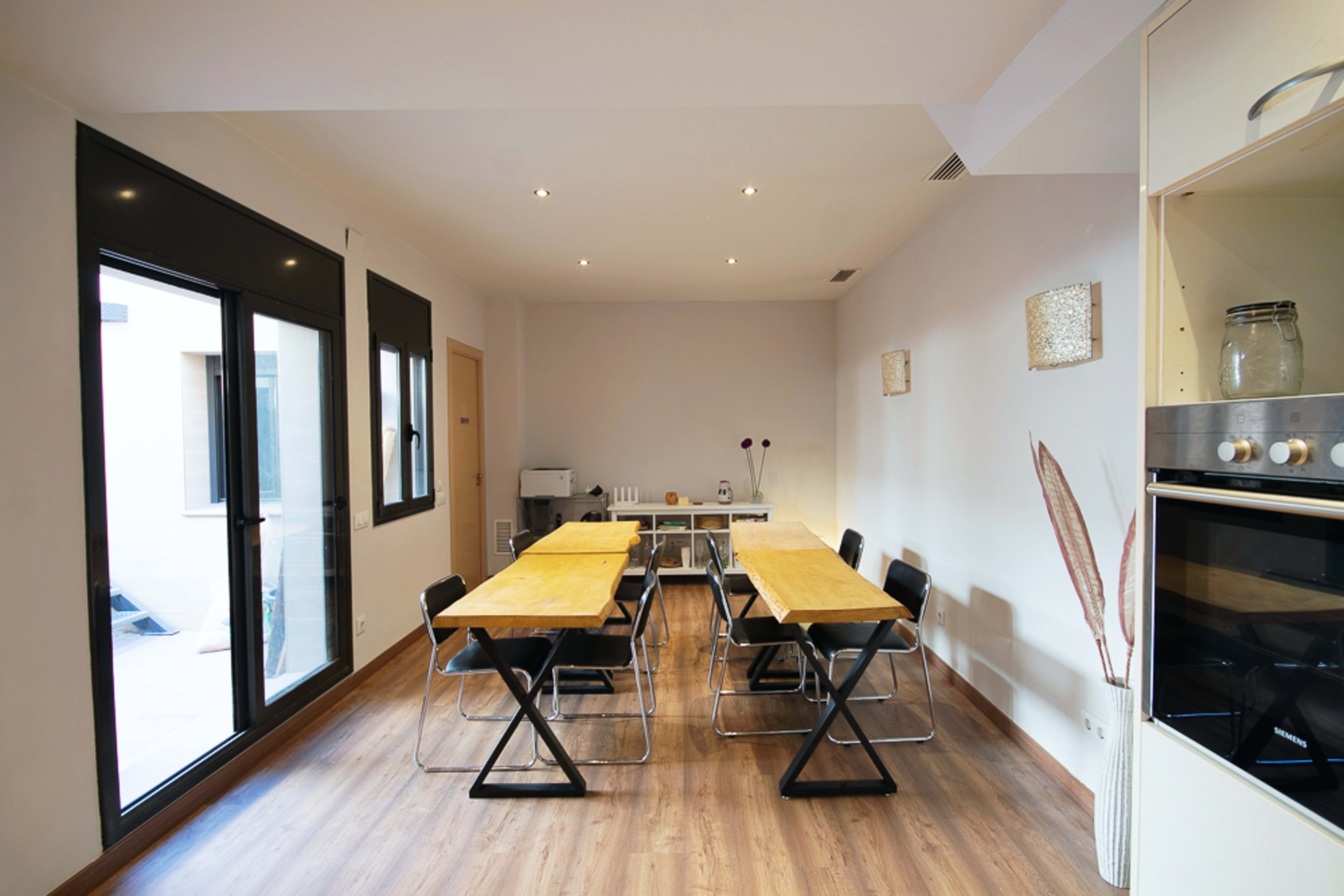 A spacious dining area features multiple wooden tables and black chairs, with large windows allowing natural light to enter.
