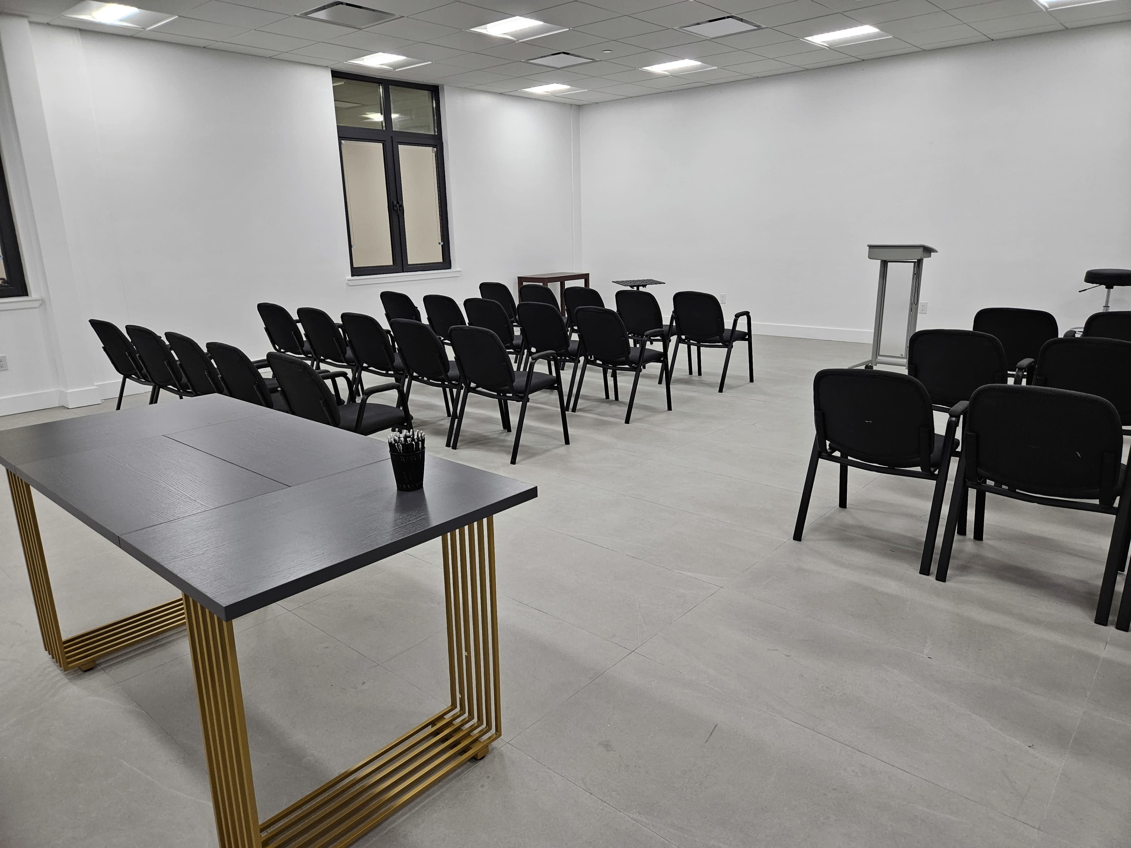 The image shows a modern, empty conference room with black chairs arranged in rows and a table with a gold base positioned to one side.