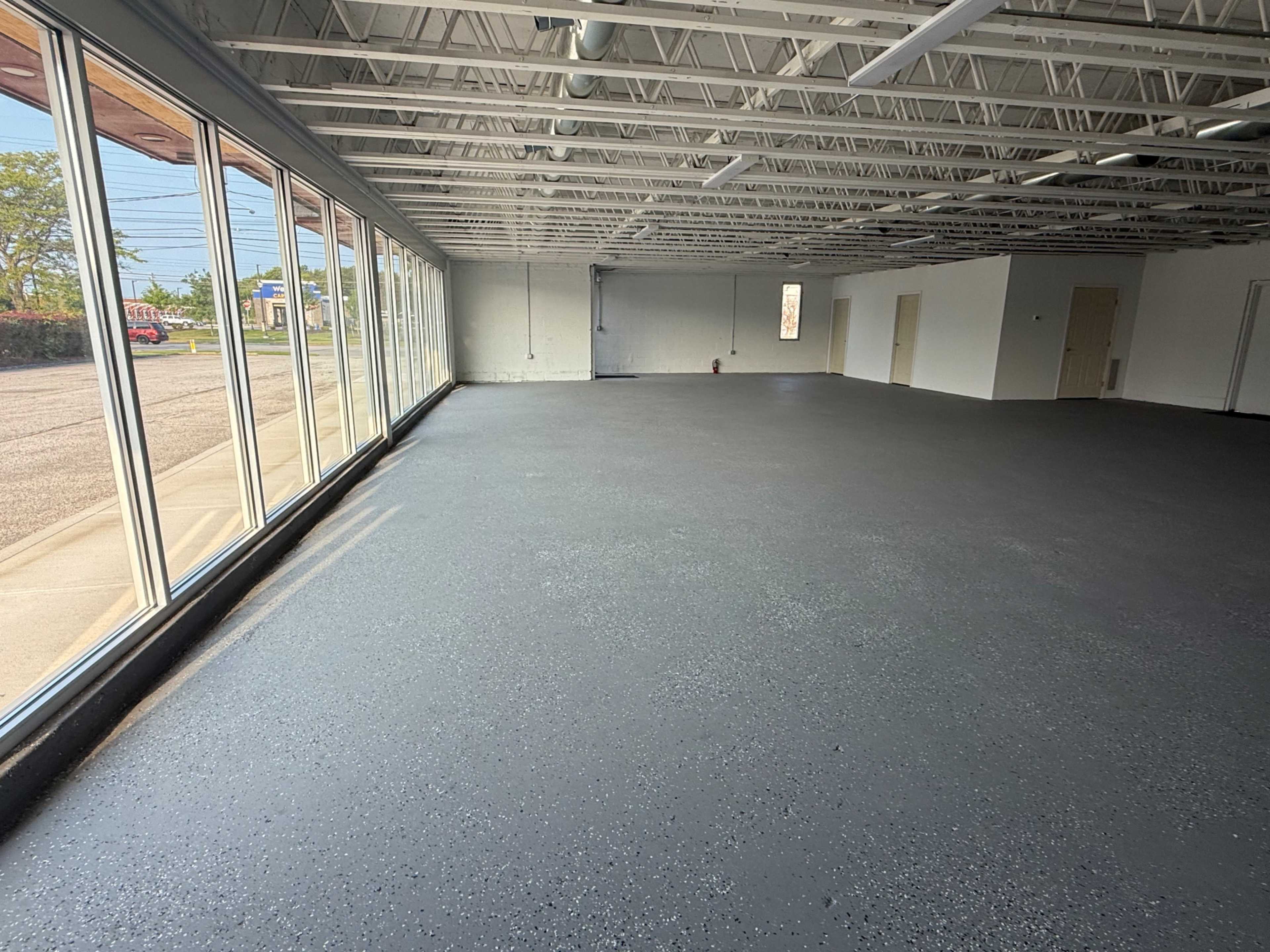 The image shows a spacious, empty commercial interior with a smooth, dark floor and large windows along one wall.