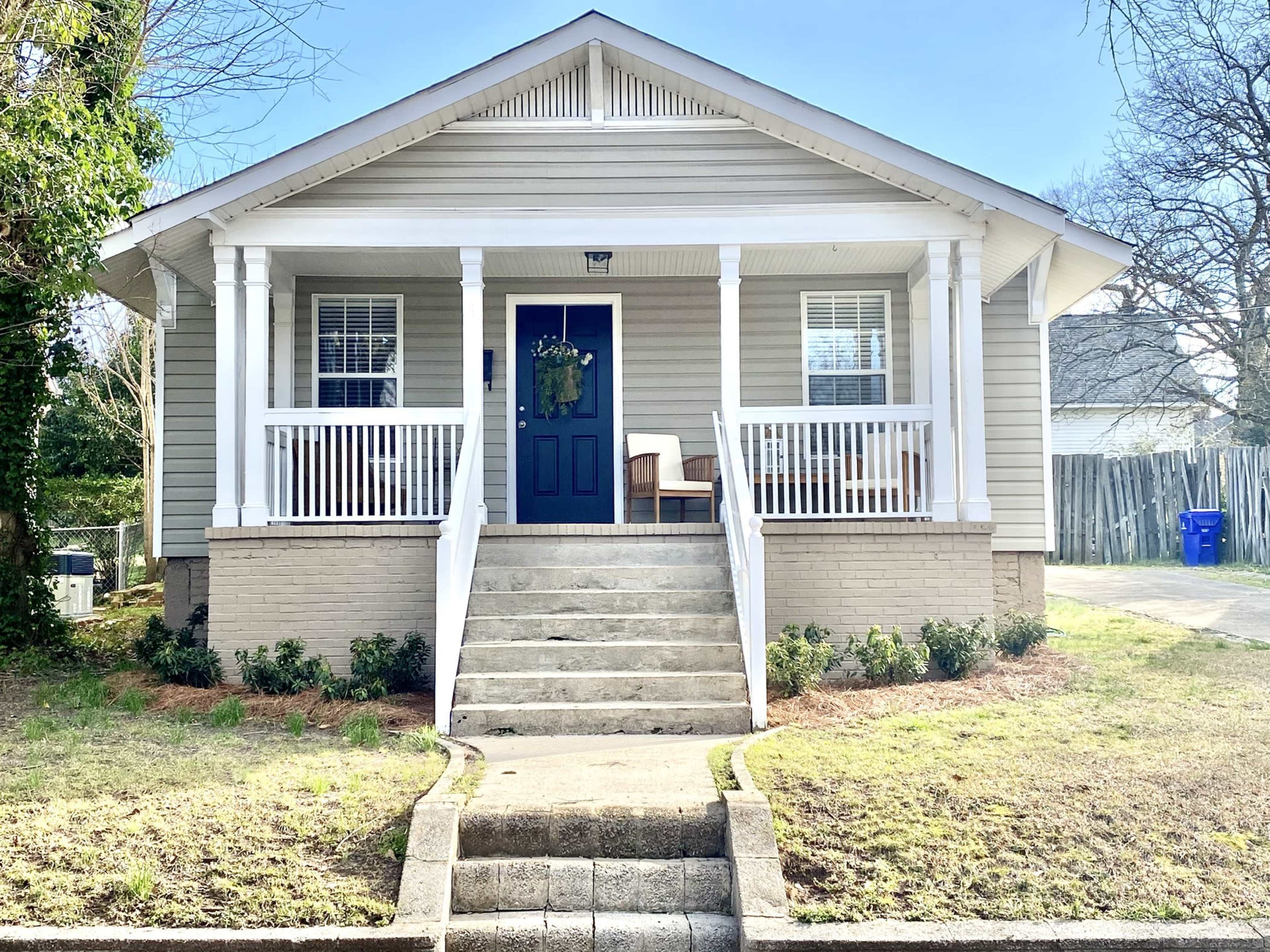 A two-story house with a front porch, white columns, and a dark blue door, surrounded by a lawn and walkways.