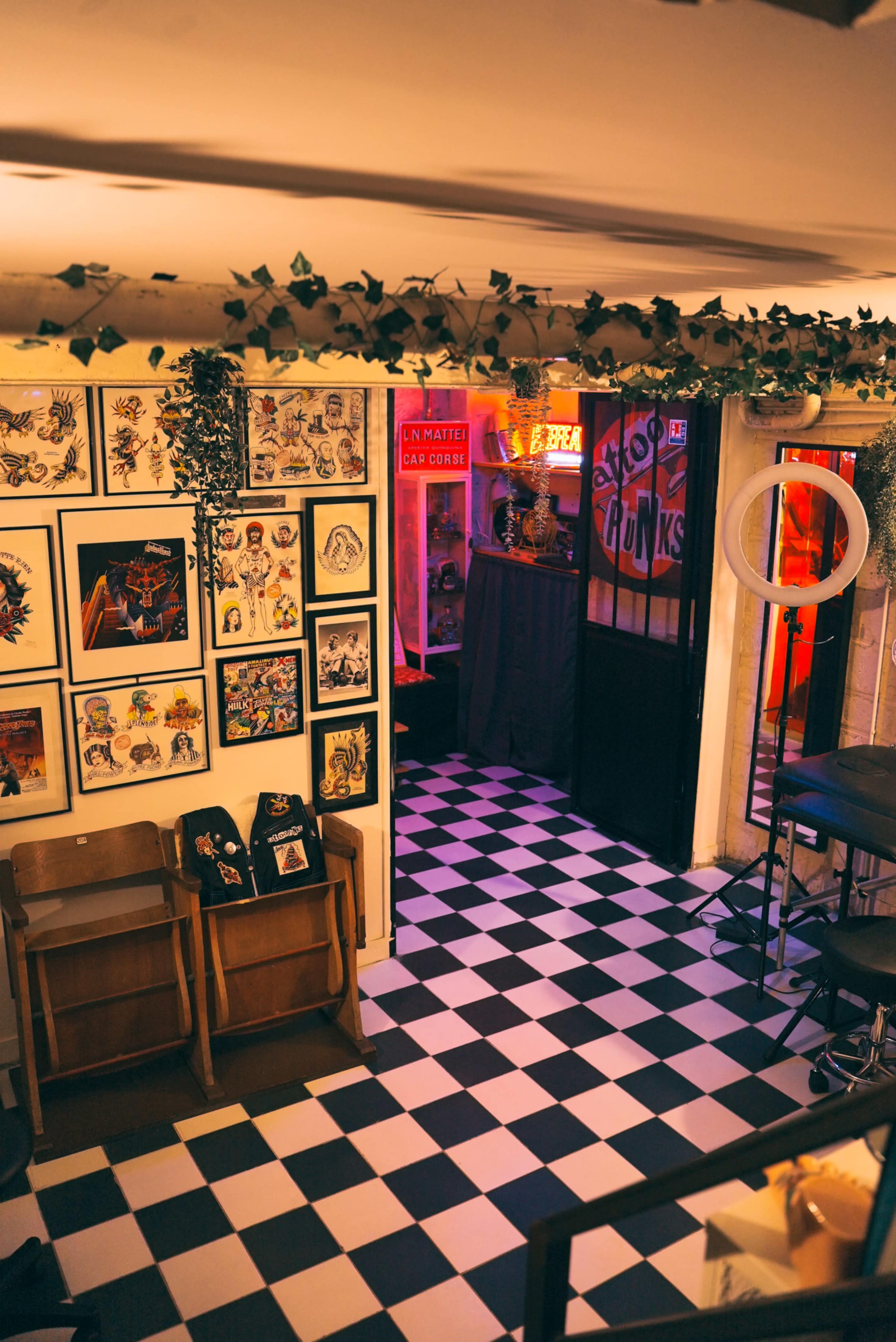 The interior of a cafe featuring a black-and-white checkered floor, framed artwork on the walls, and a dimly lit doorway leading to a separate area.