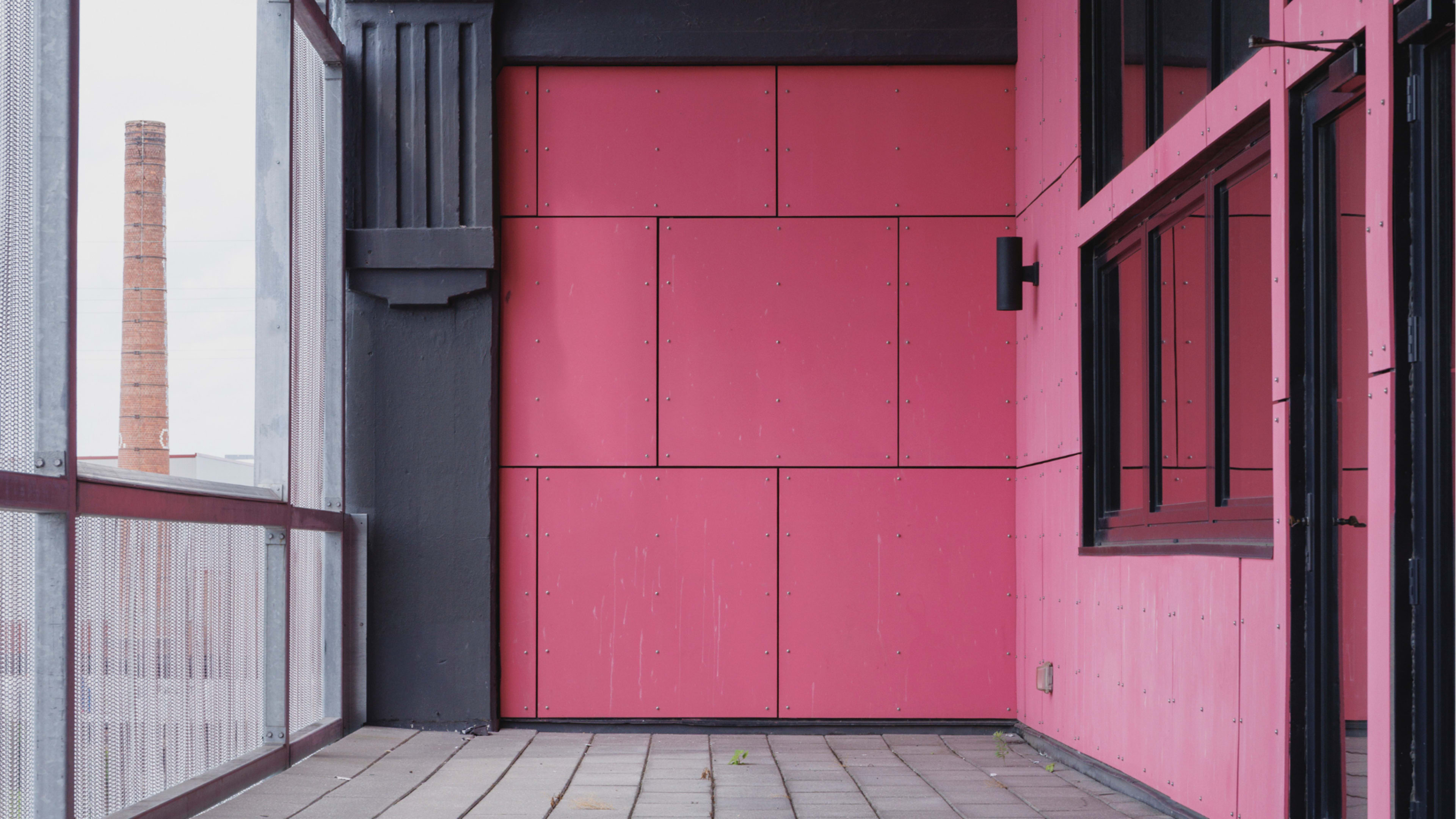 The image shows a balcony with pink walls and a visible brick chimney in the background.