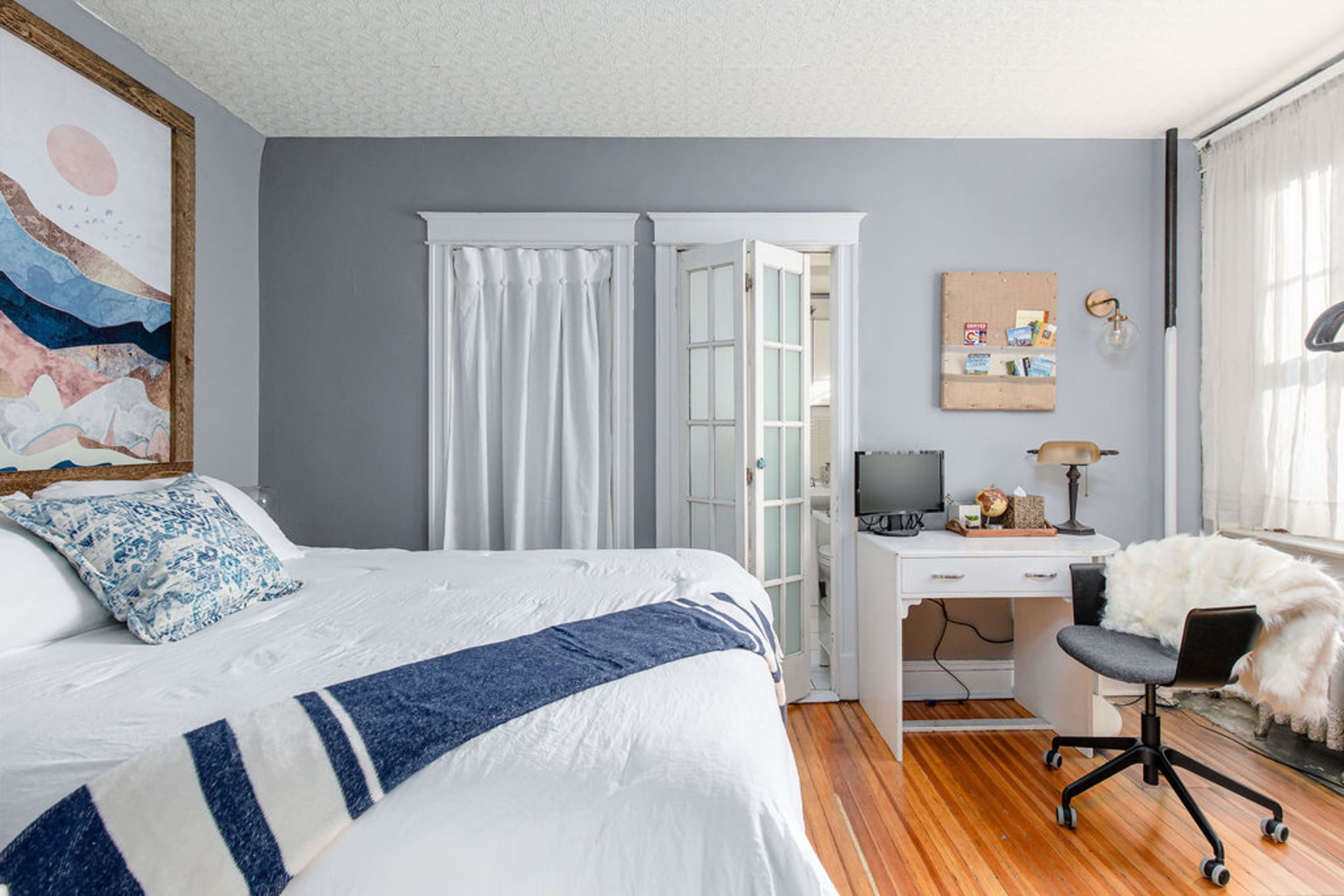 A cozy bedroom with a large bed, a desk with a computer, and a closet with double doors, all featuring a soft color palette.