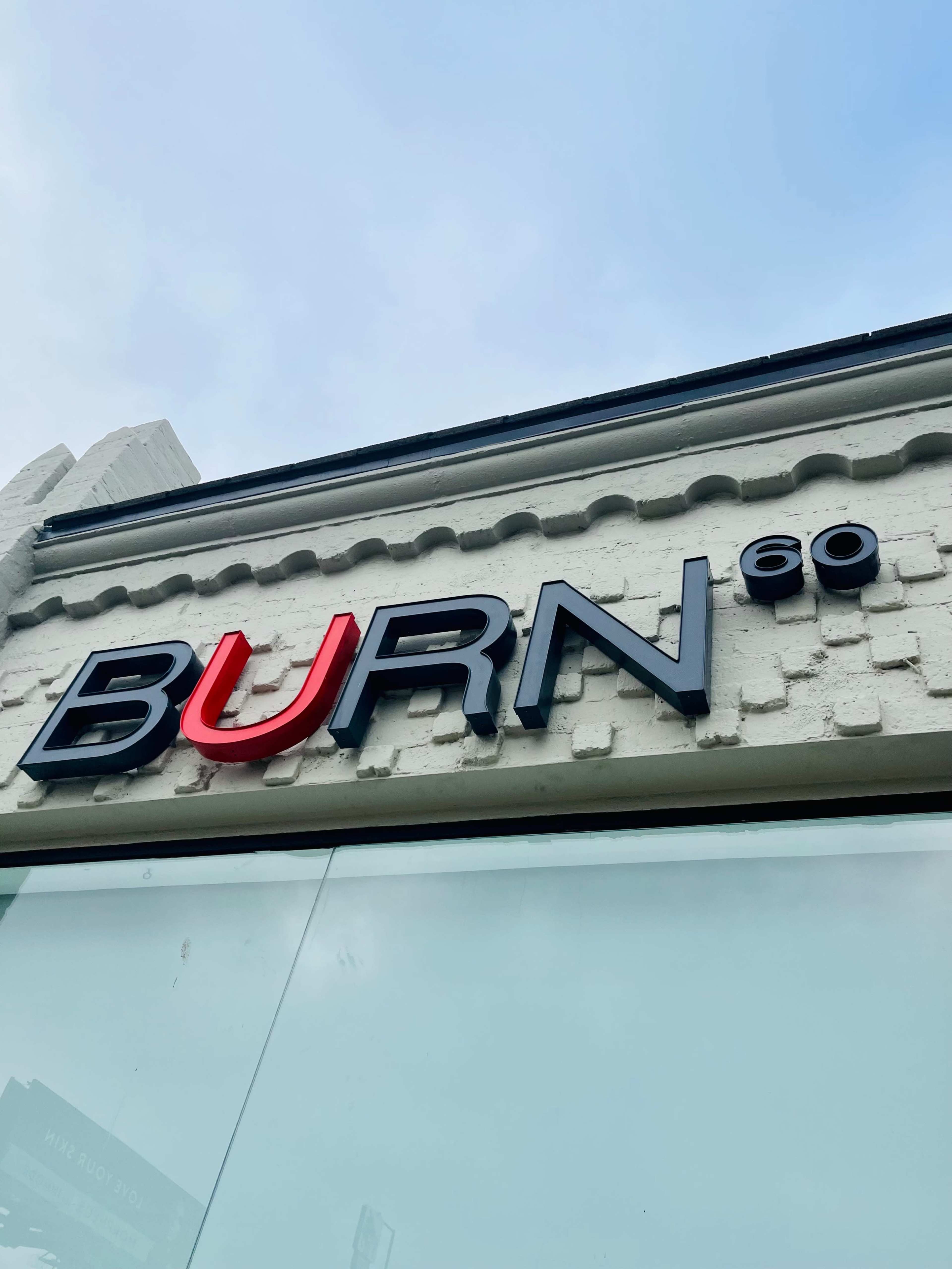 The image shows the sign of a fitness studio called "BURN60" mounted on a white brick wall under a clear sky.