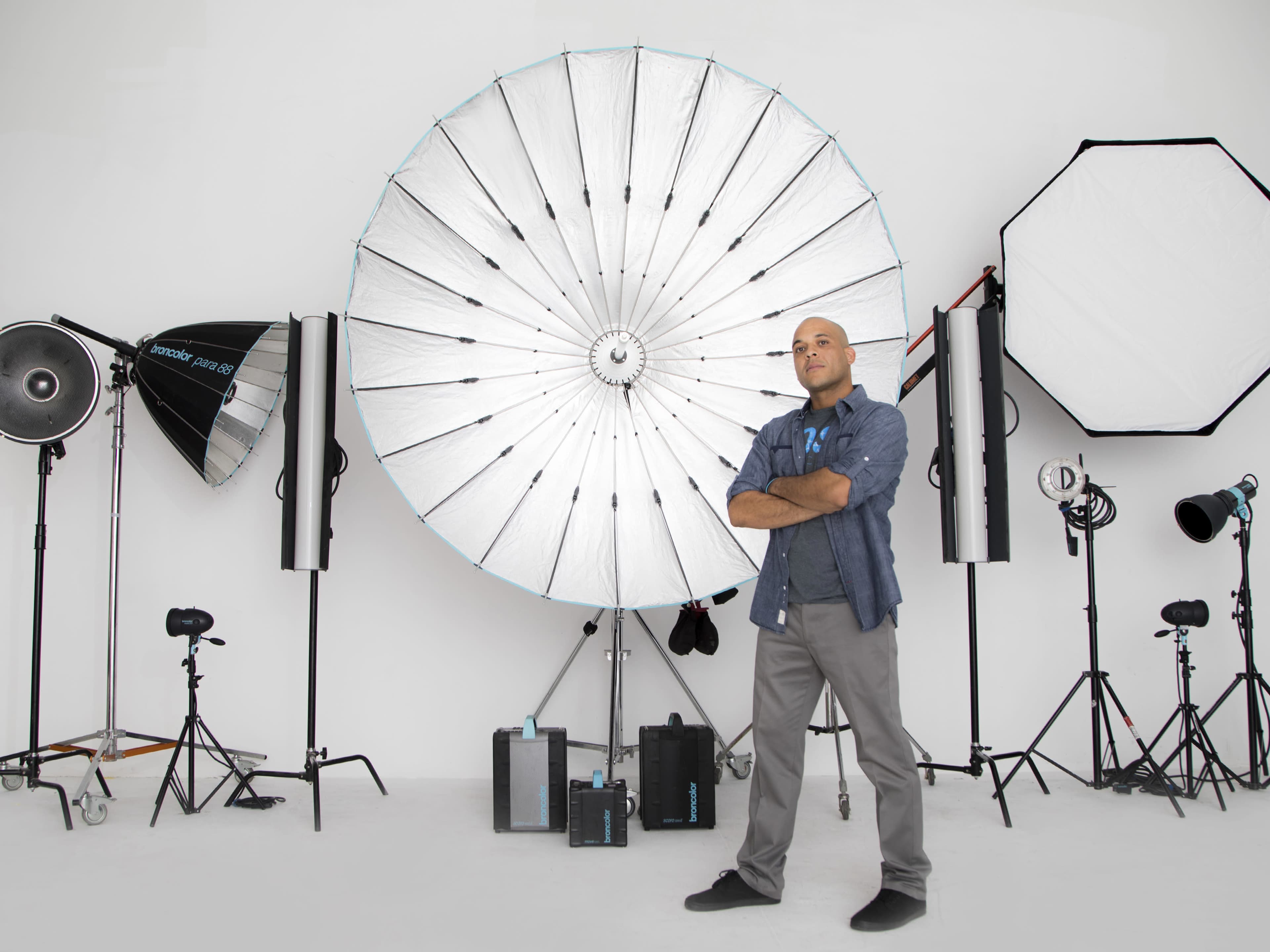 A man stands confidently in front of various photography lighting equipment arranged in a studio setting.