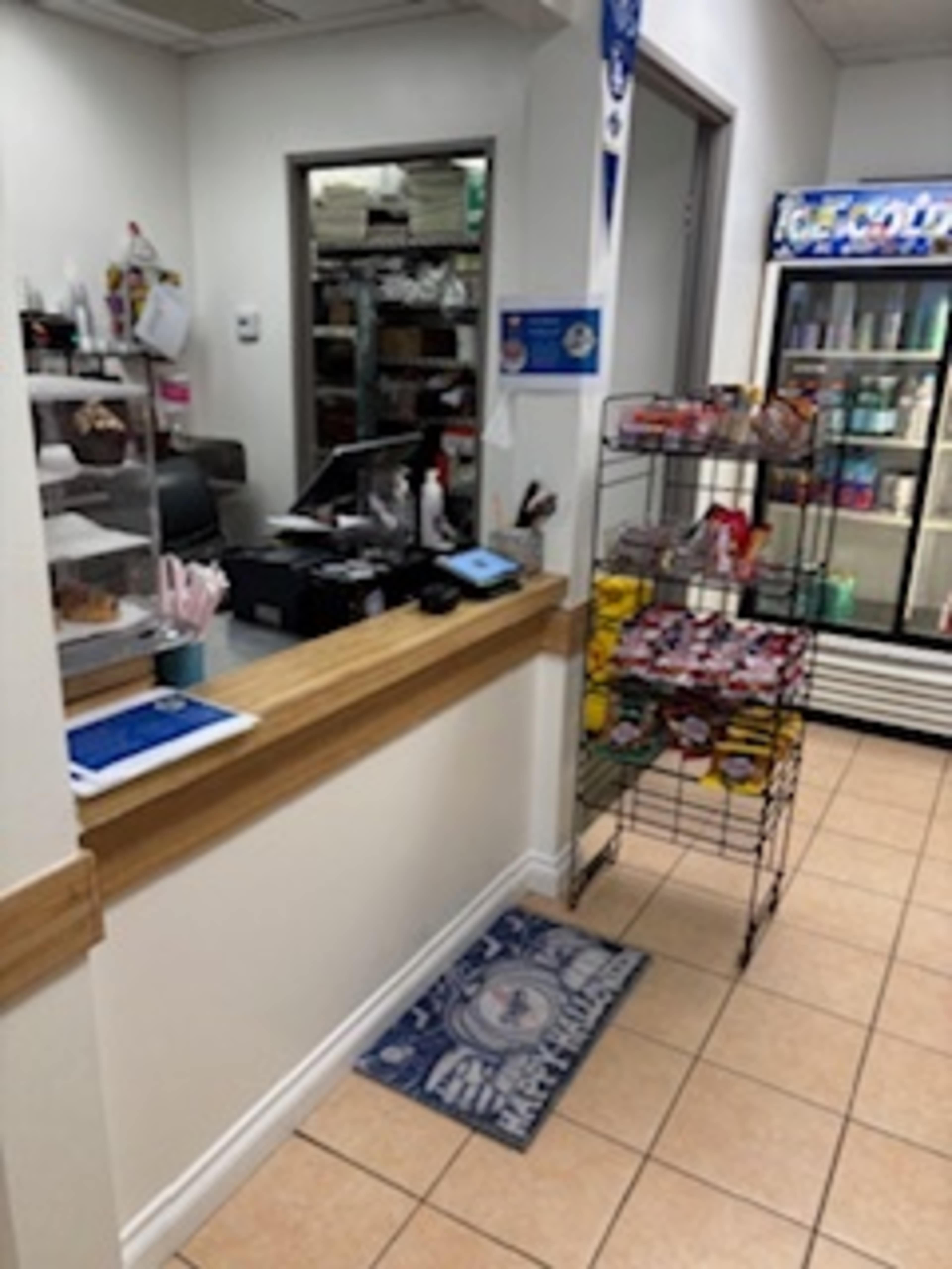 The image shows a reception area with a counter, a cash register, and a display rack filled with snacks next to a refrigerator.