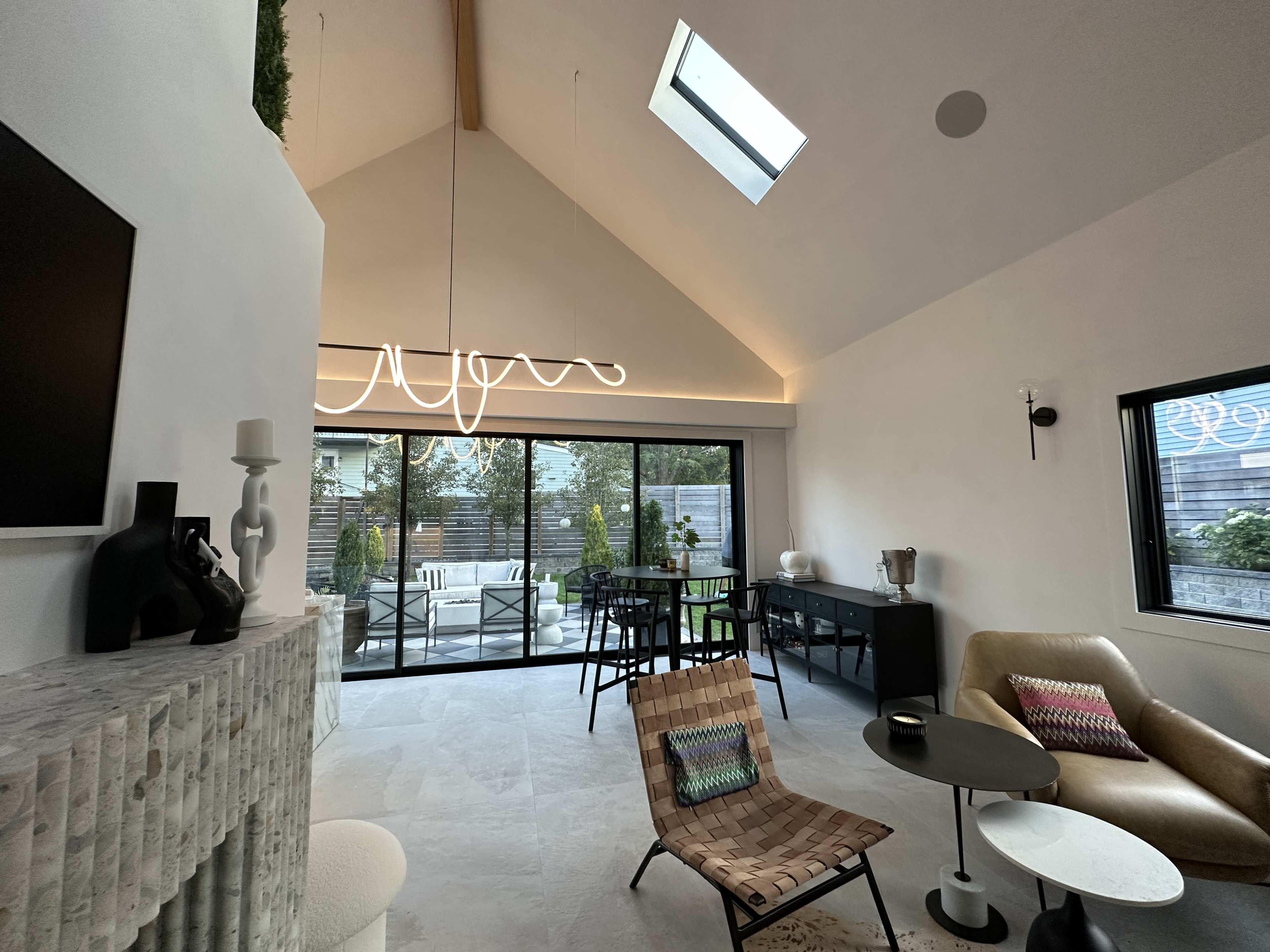 A modern living space featuring a minimalistic interior design with a large glass door leading to a patio, a stylish light fixture, and a blend of contemporary furniture.
