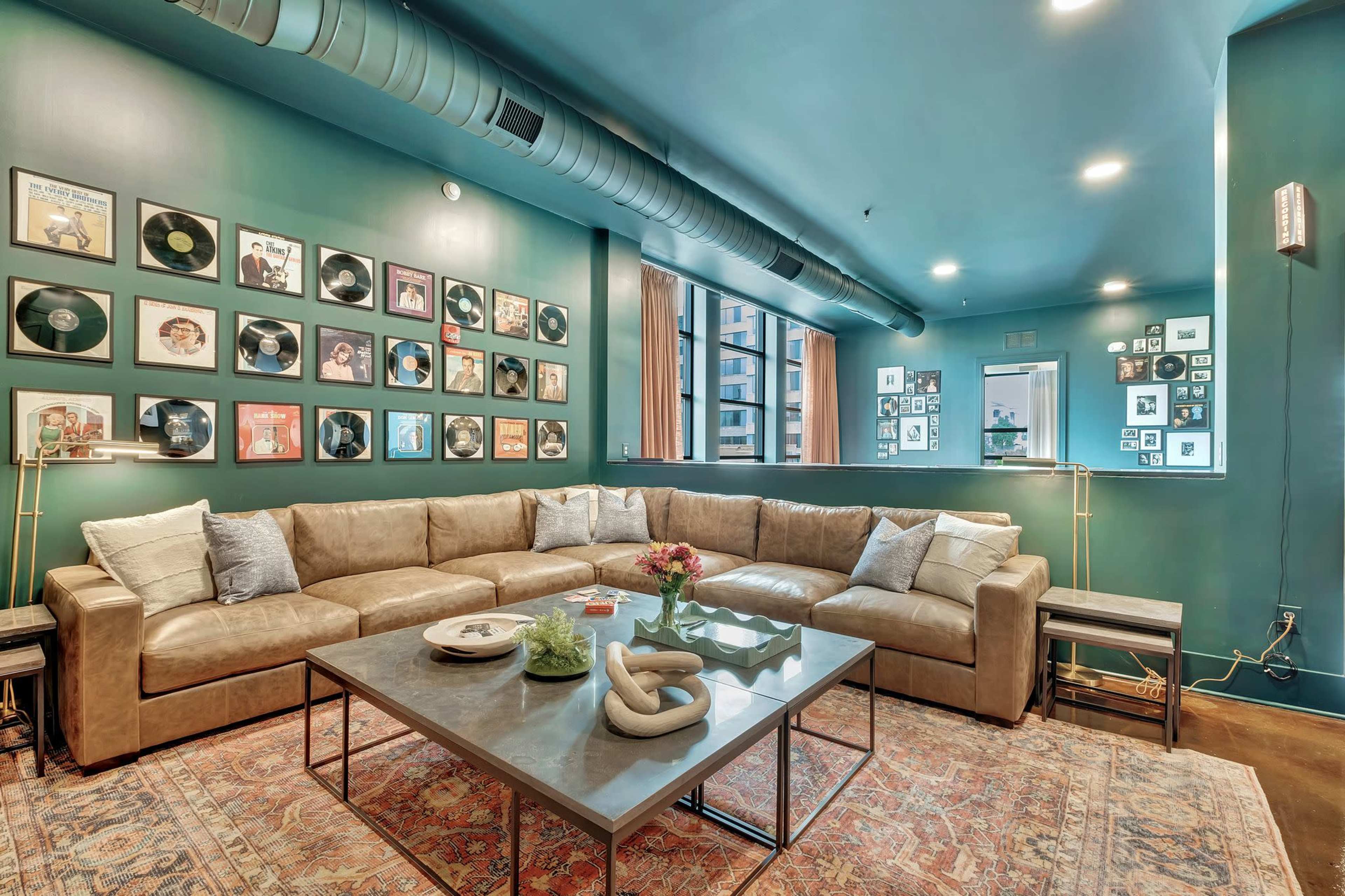 A spacious living room features a large sectional sofa, a coffee table with decorative items, and walls adorned with framed records and photographs.