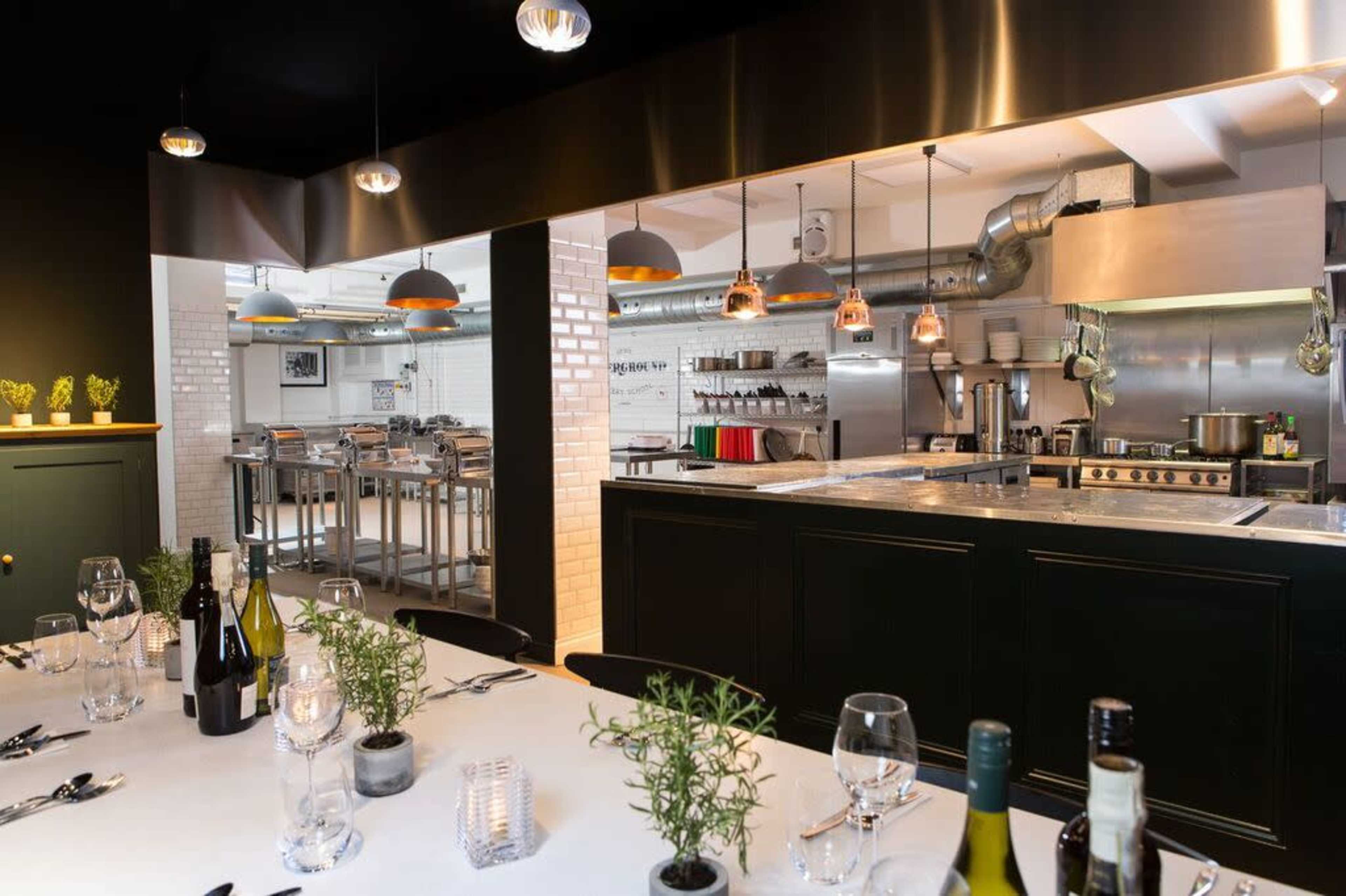 A modern kitchen with stainless steel appliances is visible behind a dining area set with a white tablecloth, wine bottles, and decorative herbs.