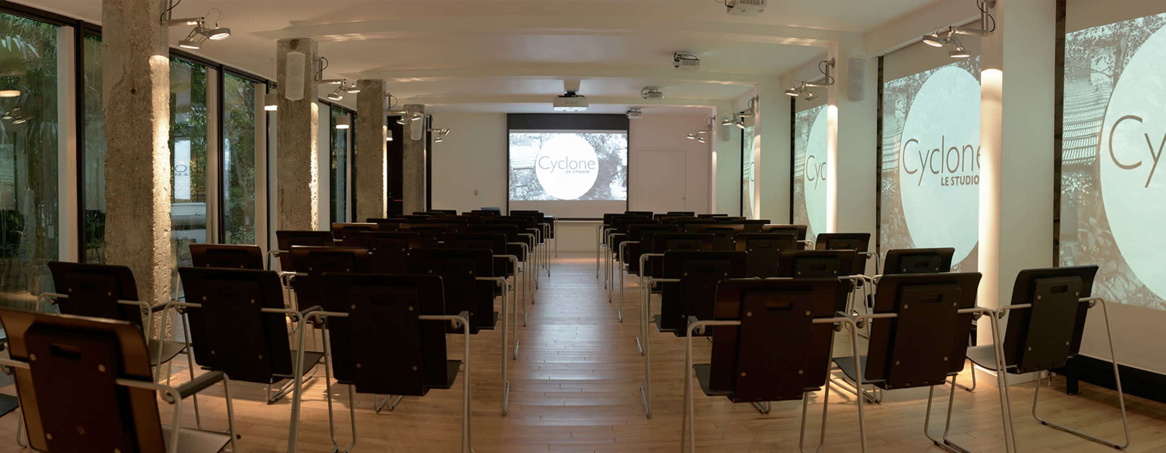 The image shows a modern conference room with rows of chairs facing a projector screen displaying the word "Cyclone."