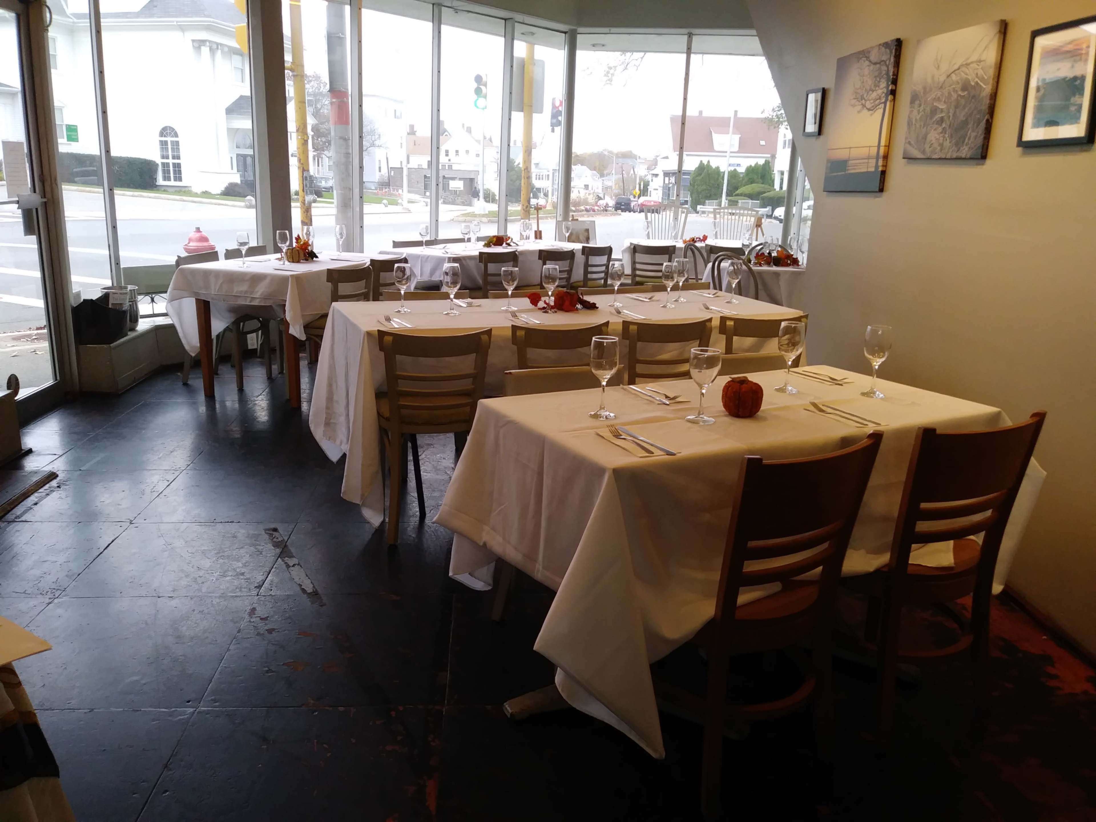 The image shows a restaurant interior with white tablecloths on several tables arranged in a corner, and large windows overlooking a street outside.