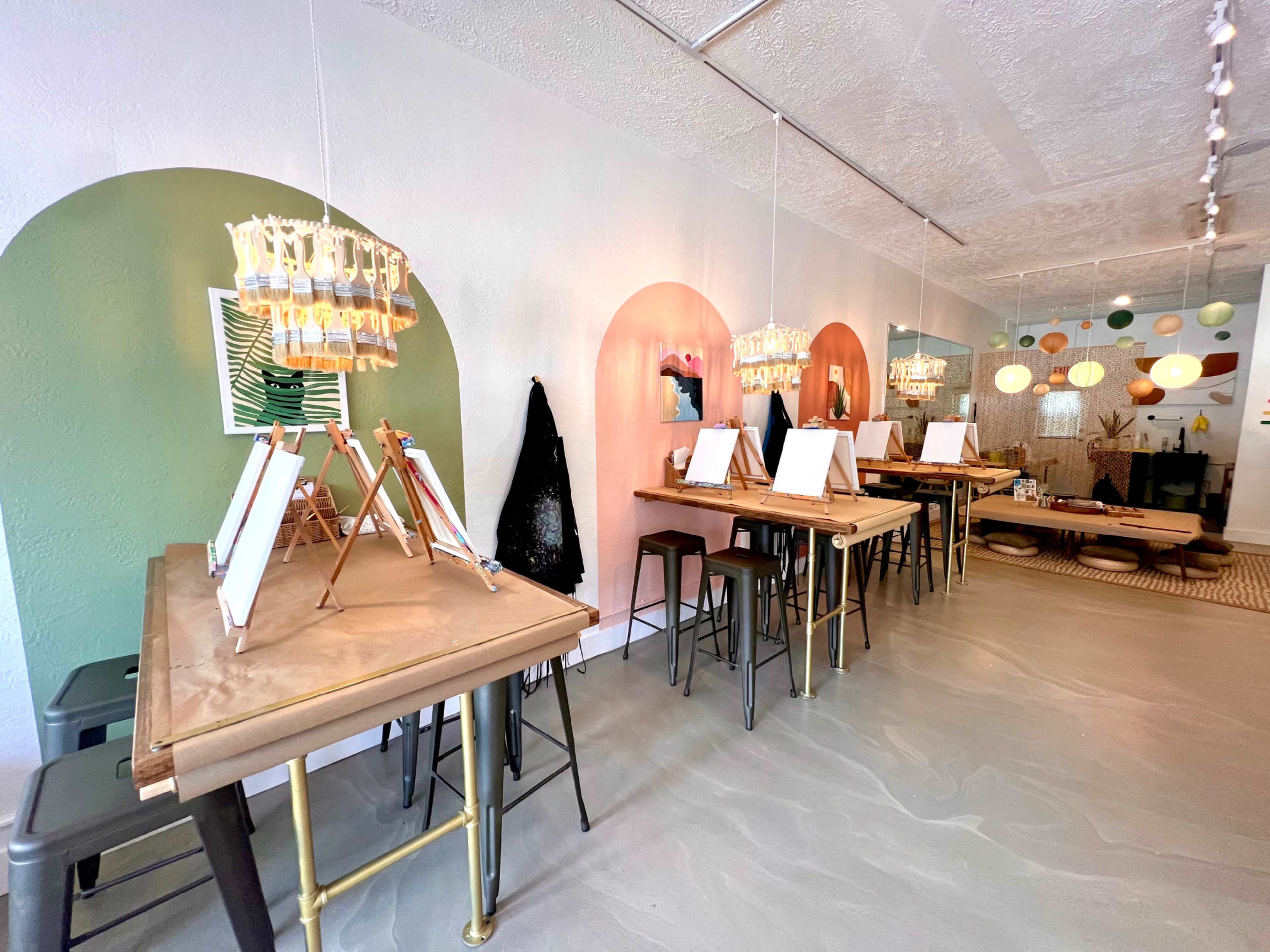 An art studio with several tables equipped with easels, styled walls in pastel colors, and hanging light fixtures.