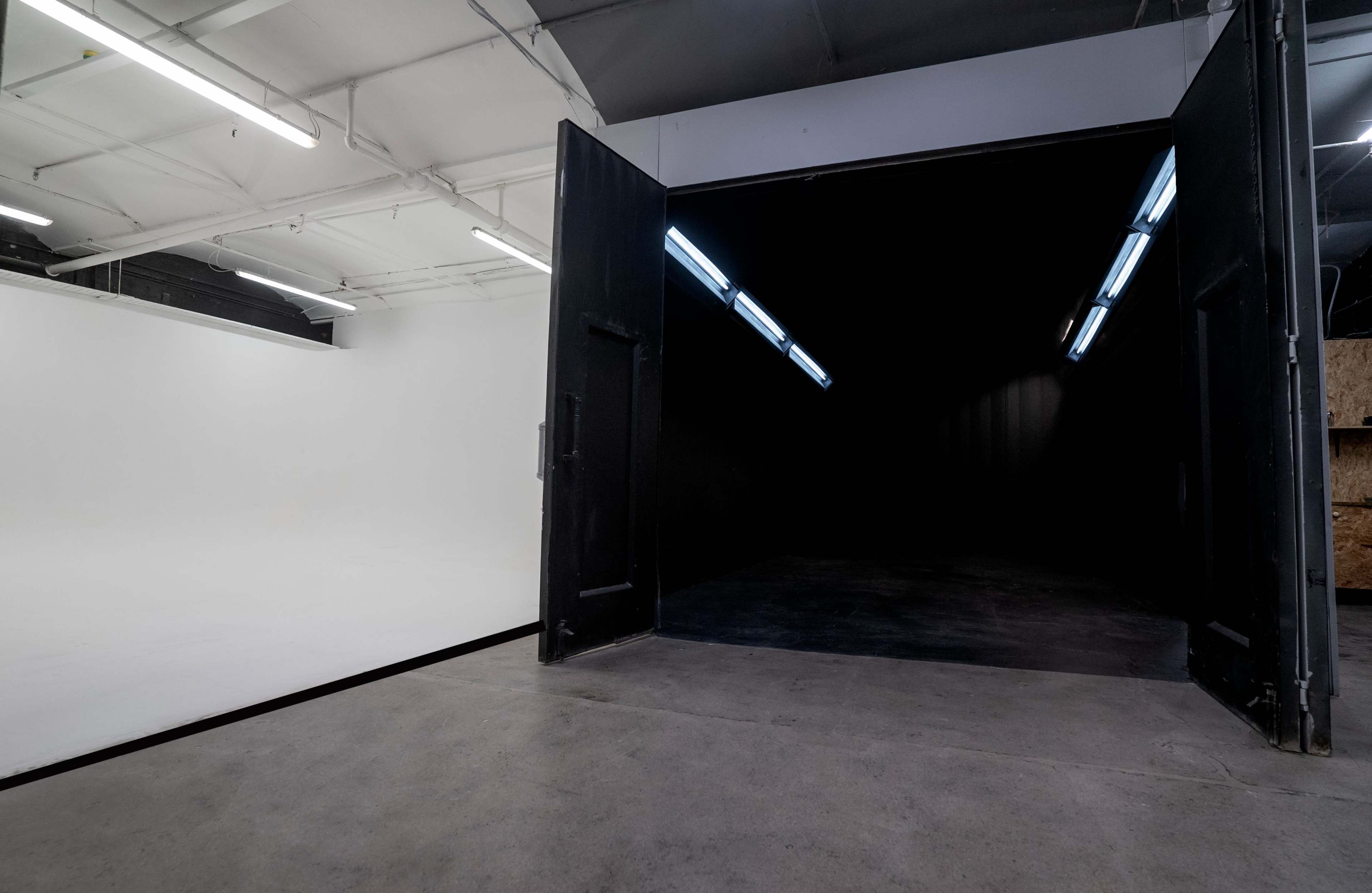 A large studio space features an open double door leading to a darkened area on one side and a brightly lit white backdrop on the other.