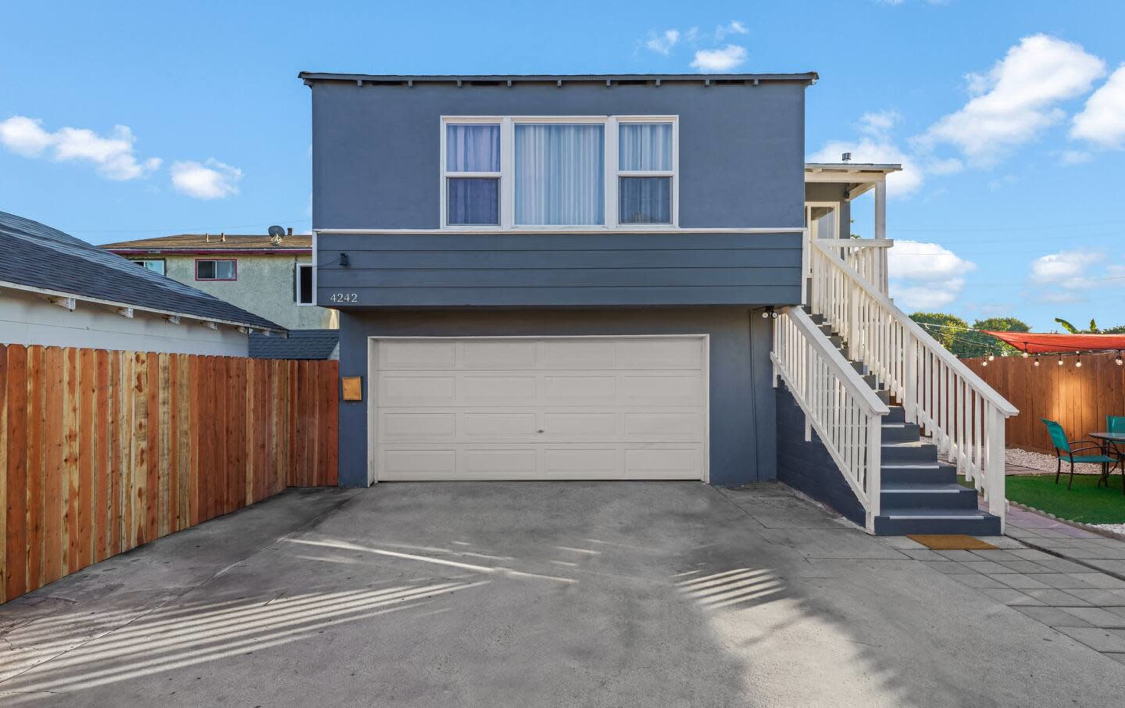 A two-story house with a garage and a staircase leading to the entrance is shown against a clear blue sky.