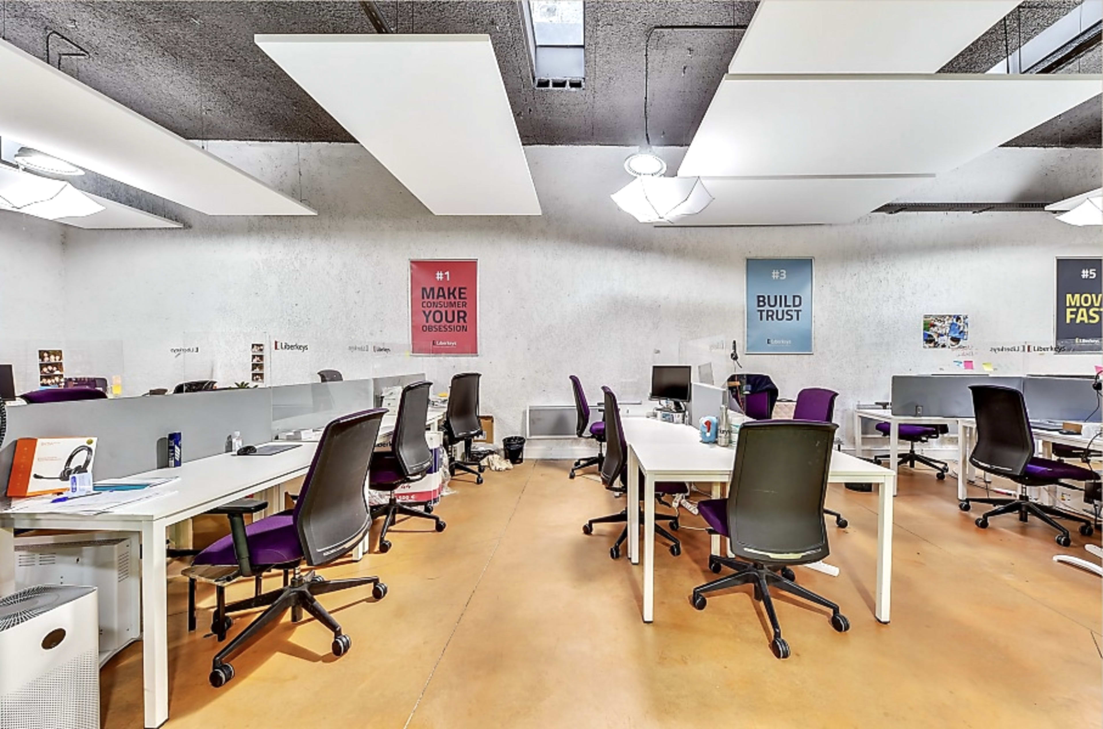 A modern office space with several white desks, black chairs, and colorful motivational posters on the walls.