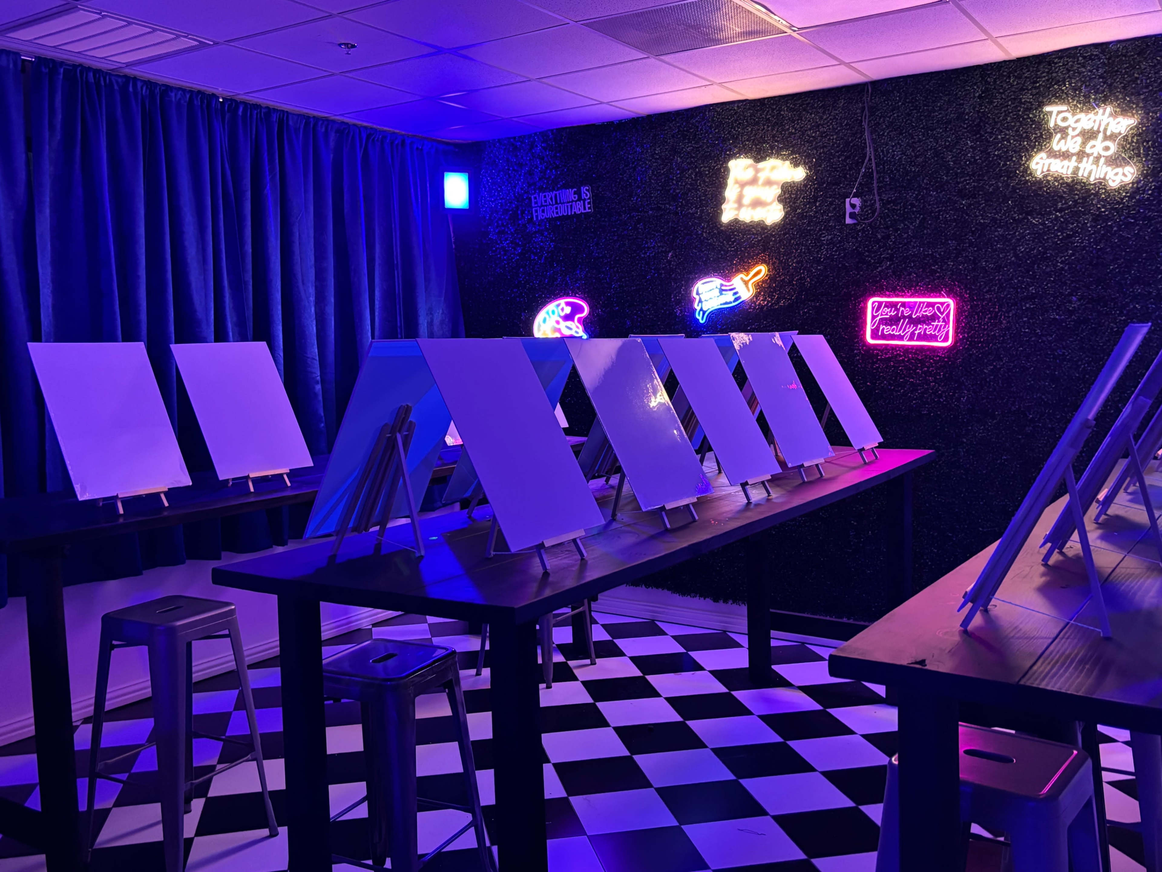 An art studio features several blank canvases on easels set against a vibrant, neon-lit wall.