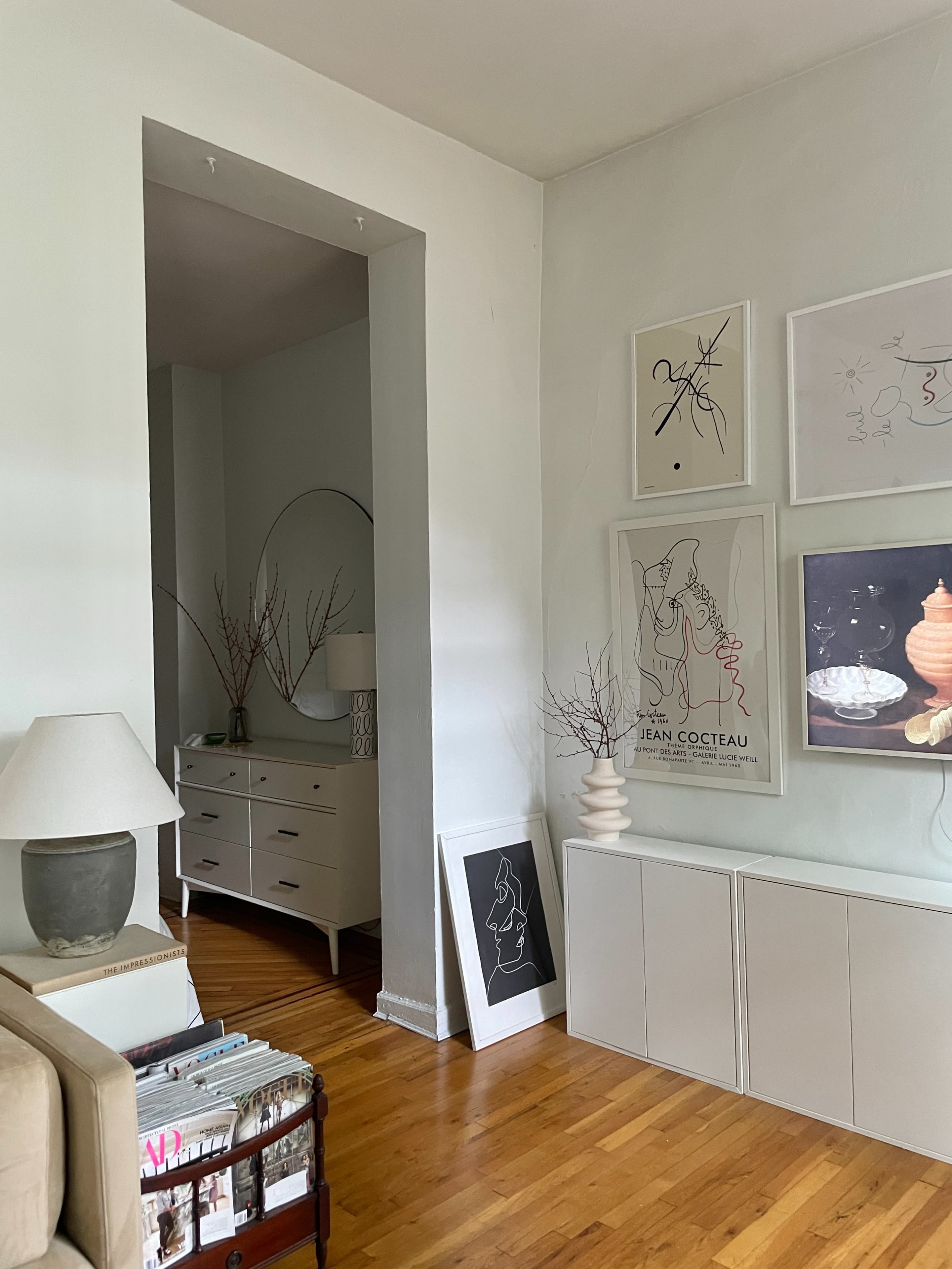 A light-filled living room features a neutral color palette, framed artworks on the walls, and a side table with decorative elements.