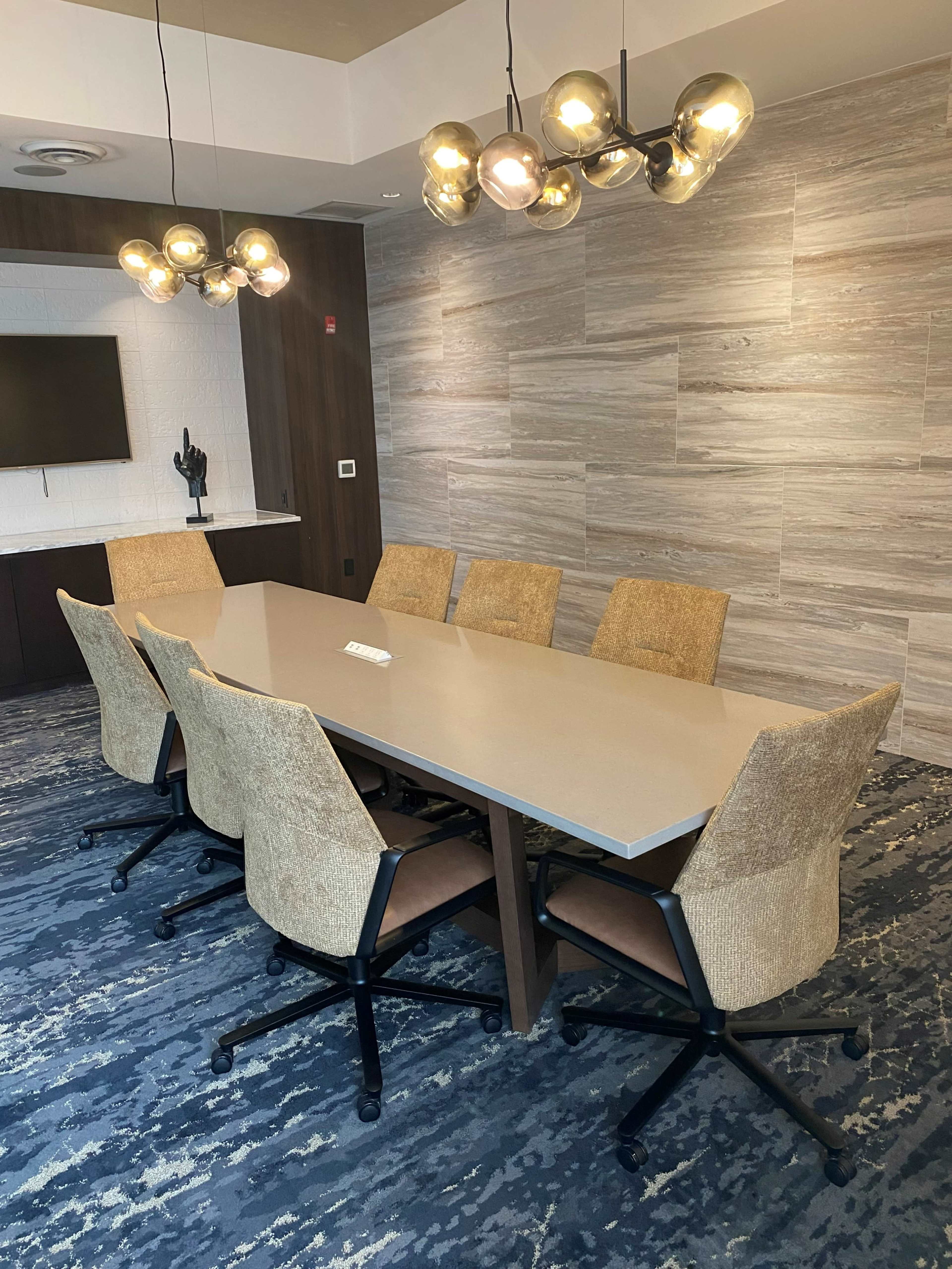 A modern conference room features a large rectangular table surrounded by six chairs, with a contemporary light fixture overhead.