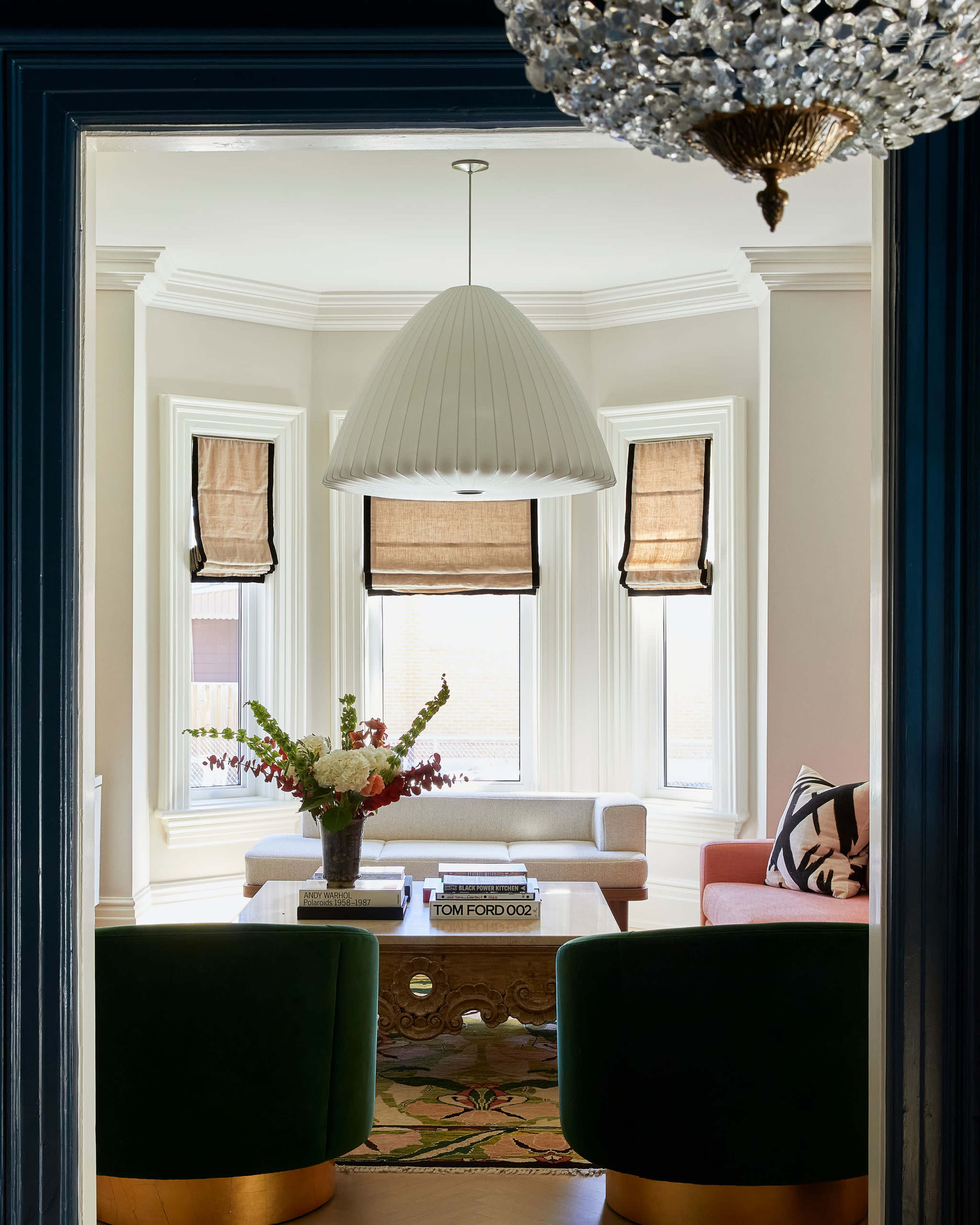 A view of a stylish living room featuring a large pendant light, a coffee table with a floral arrangement, and two green chairs.