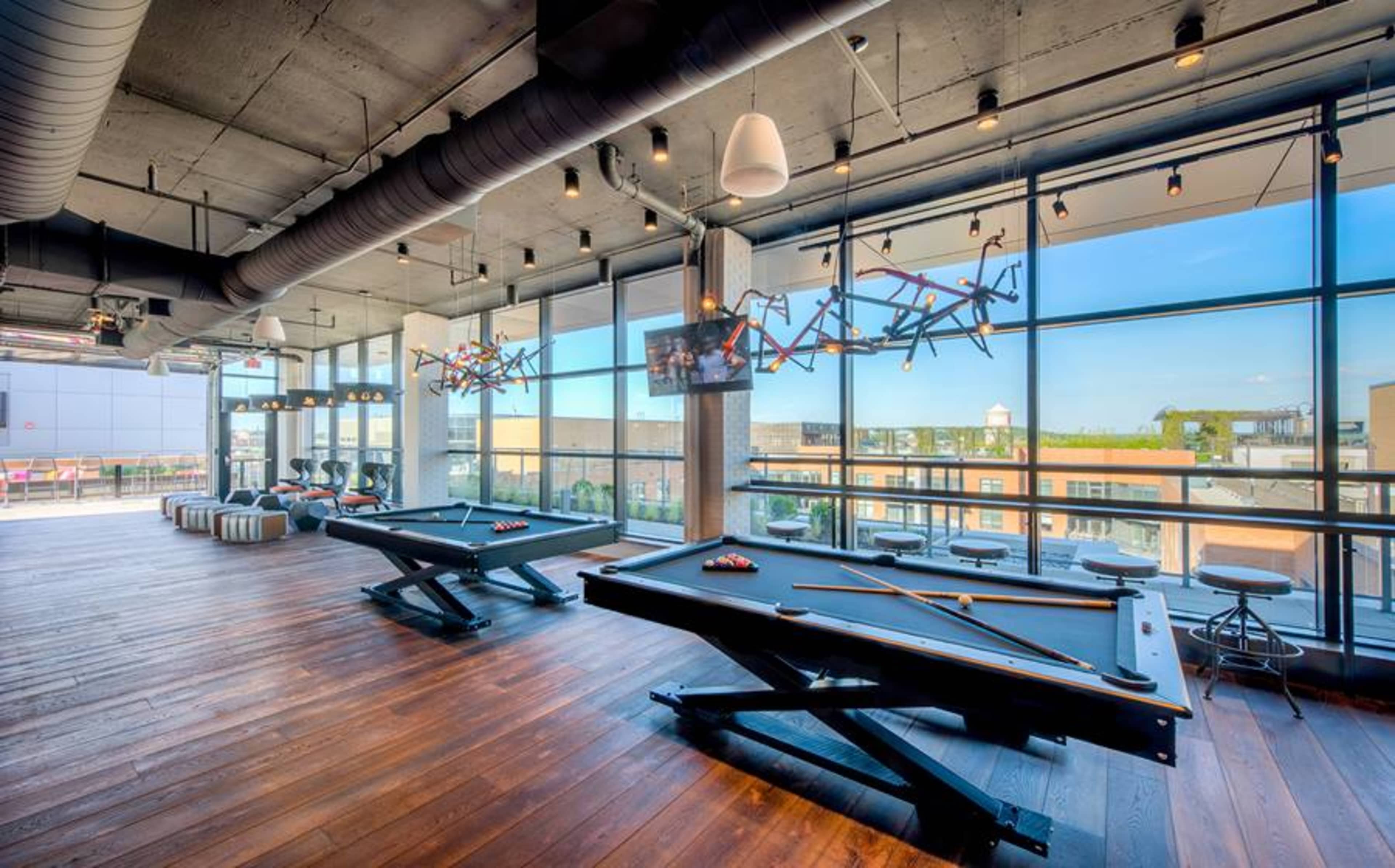 A modern game room with two pool tables, large windows, and stylish lighting fixtures.