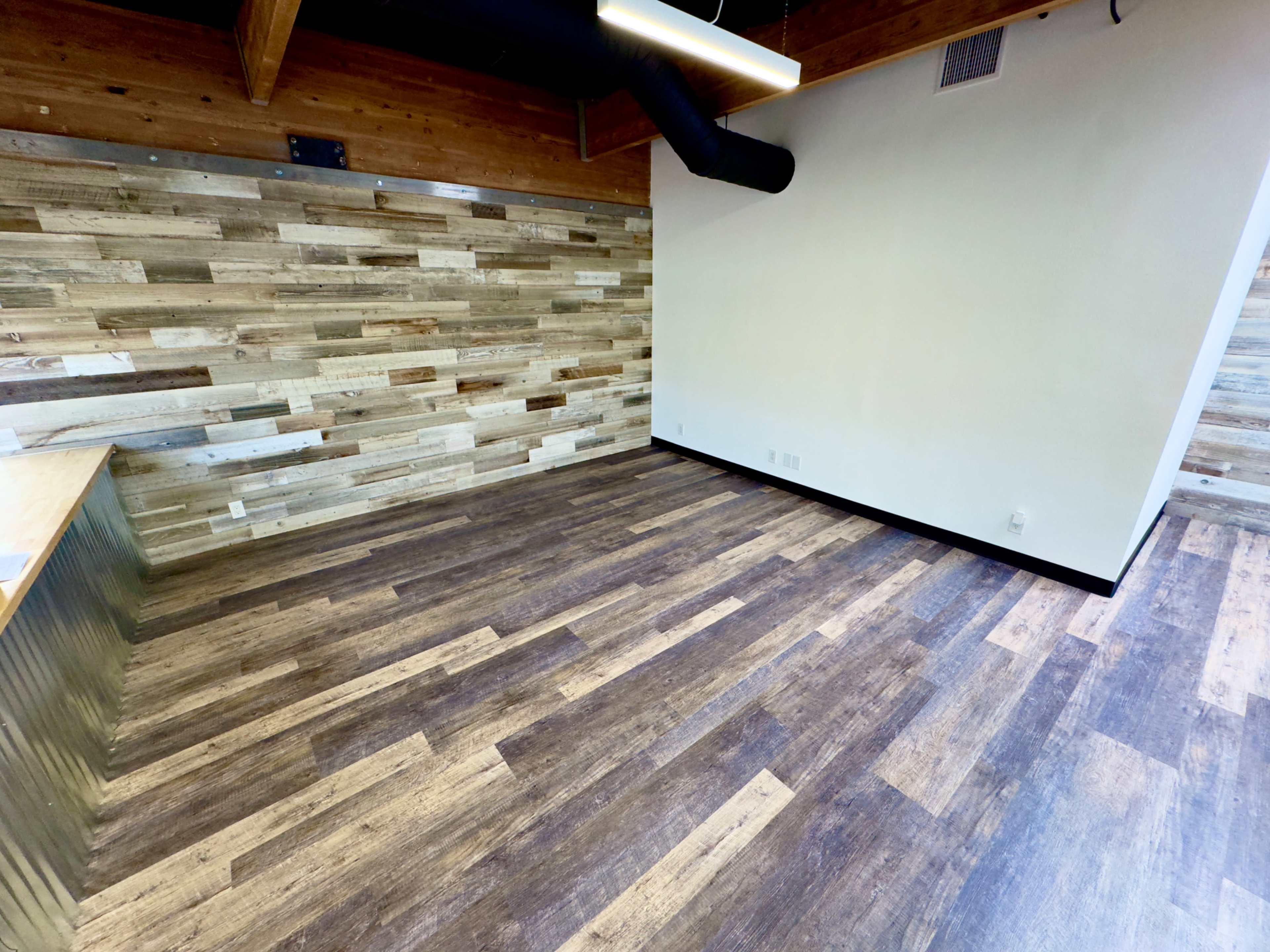 A spacious room with wooden walls, a wood-like floor, and no furniture.