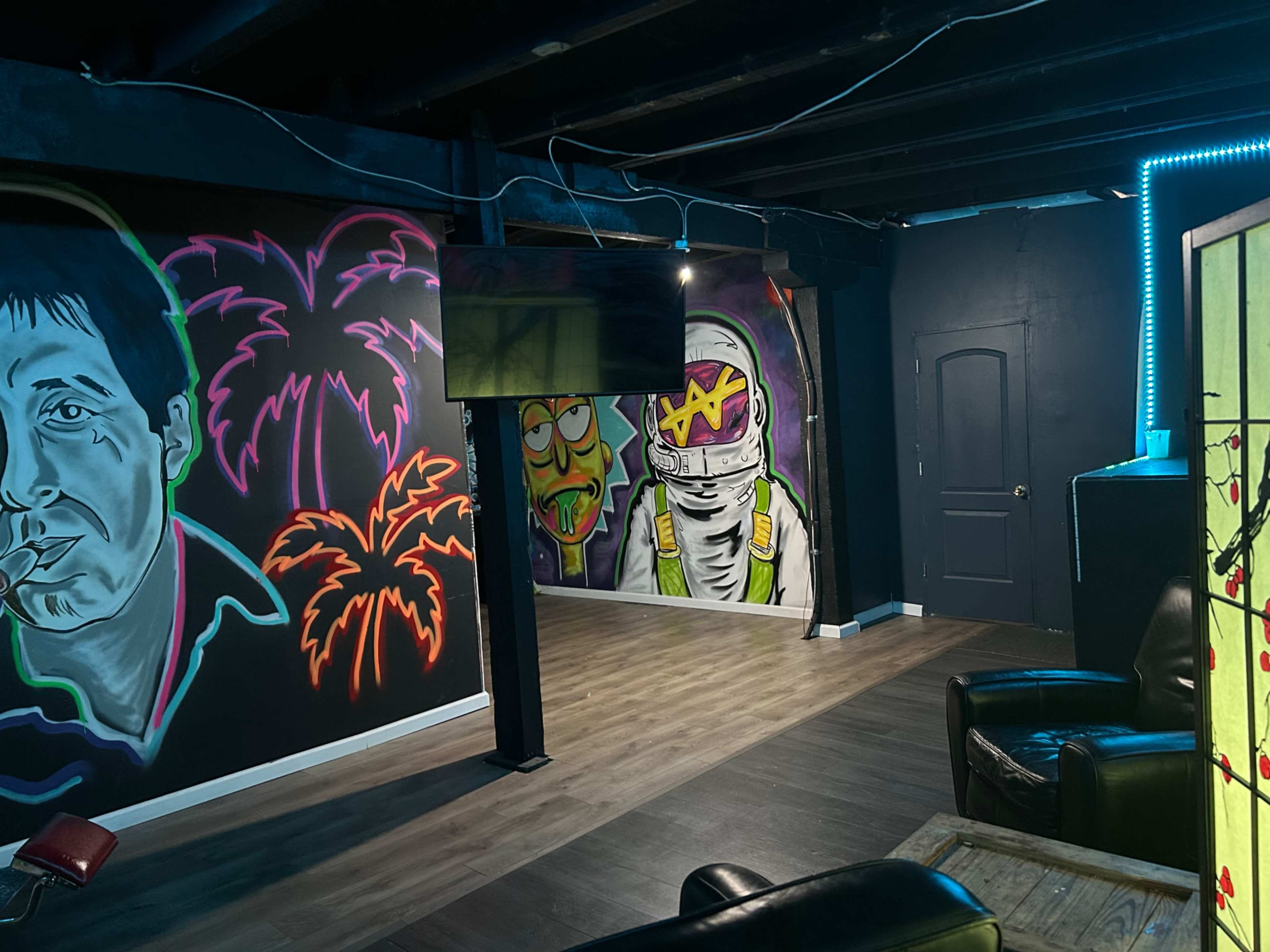 The image shows a room featuring colorful graffiti on the walls, including palm trees, a character in a space suit, and a portrait of a man.
