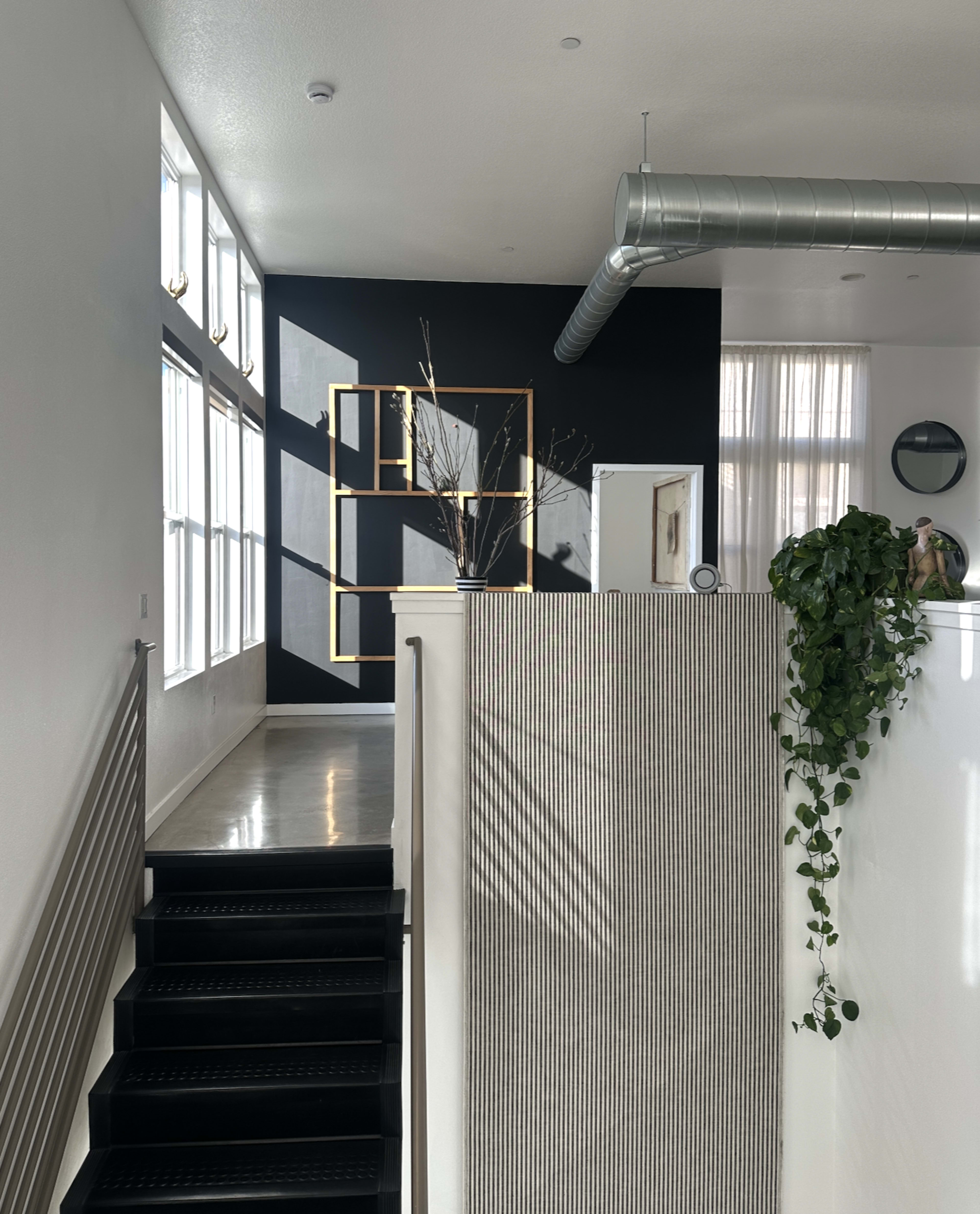 The image depicts a modern interior space featuring a staircase with black steps, a striped wall, and a dark accent wall adorned with a geometric decorative frame.