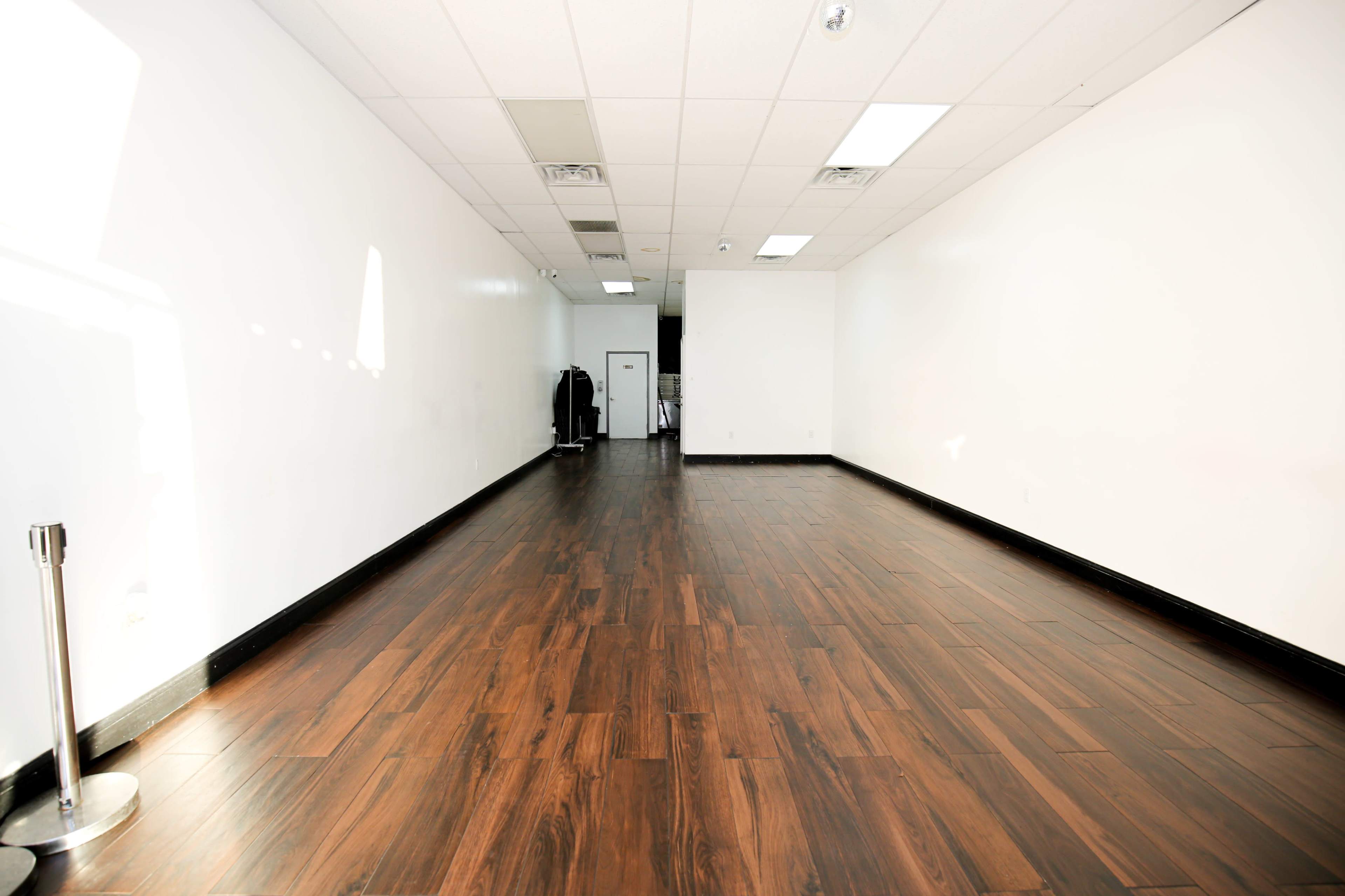 The image shows a spacious, empty retail area with wooden flooring and white walls.