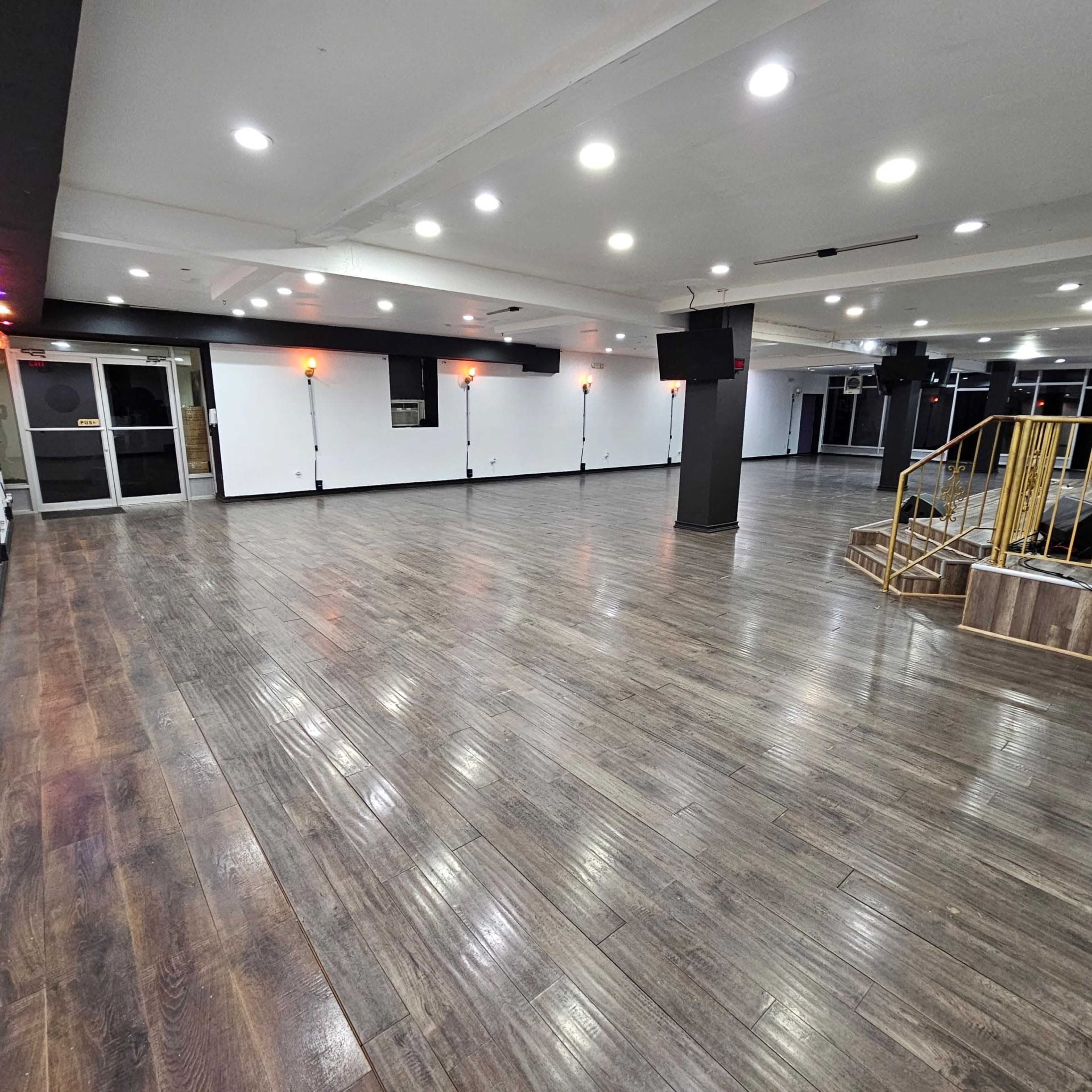 The image shows a spacious, well-lit interior of a hollow room featuring wooden flooring and multiple light fixtures on the ceiling.