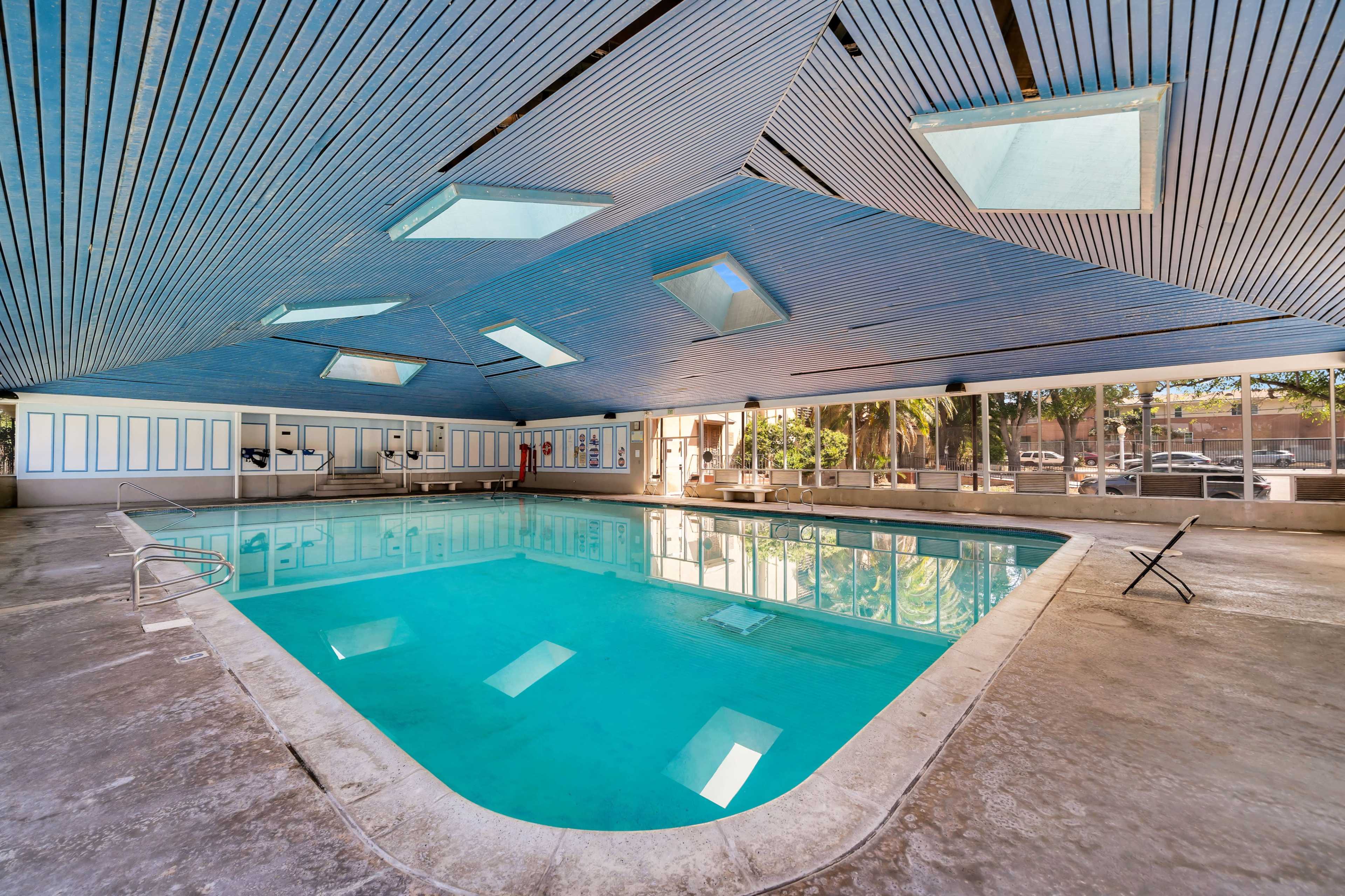 An indoor swimming pool with a distinctive ceiling design featuring skylights and large windows that overlook a garden area.