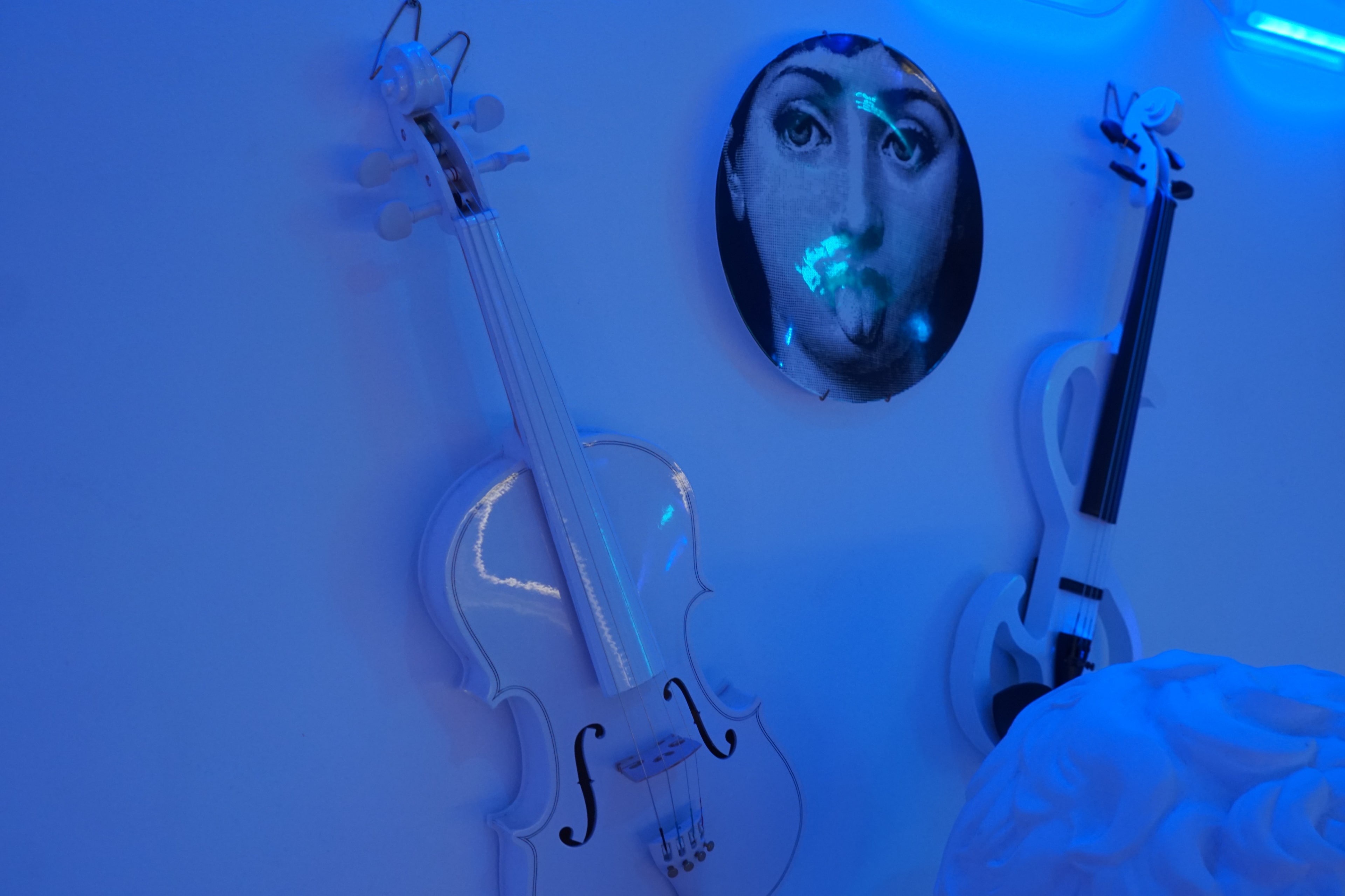 White violins and a round artwork featuring a face against a blue-lit wall.