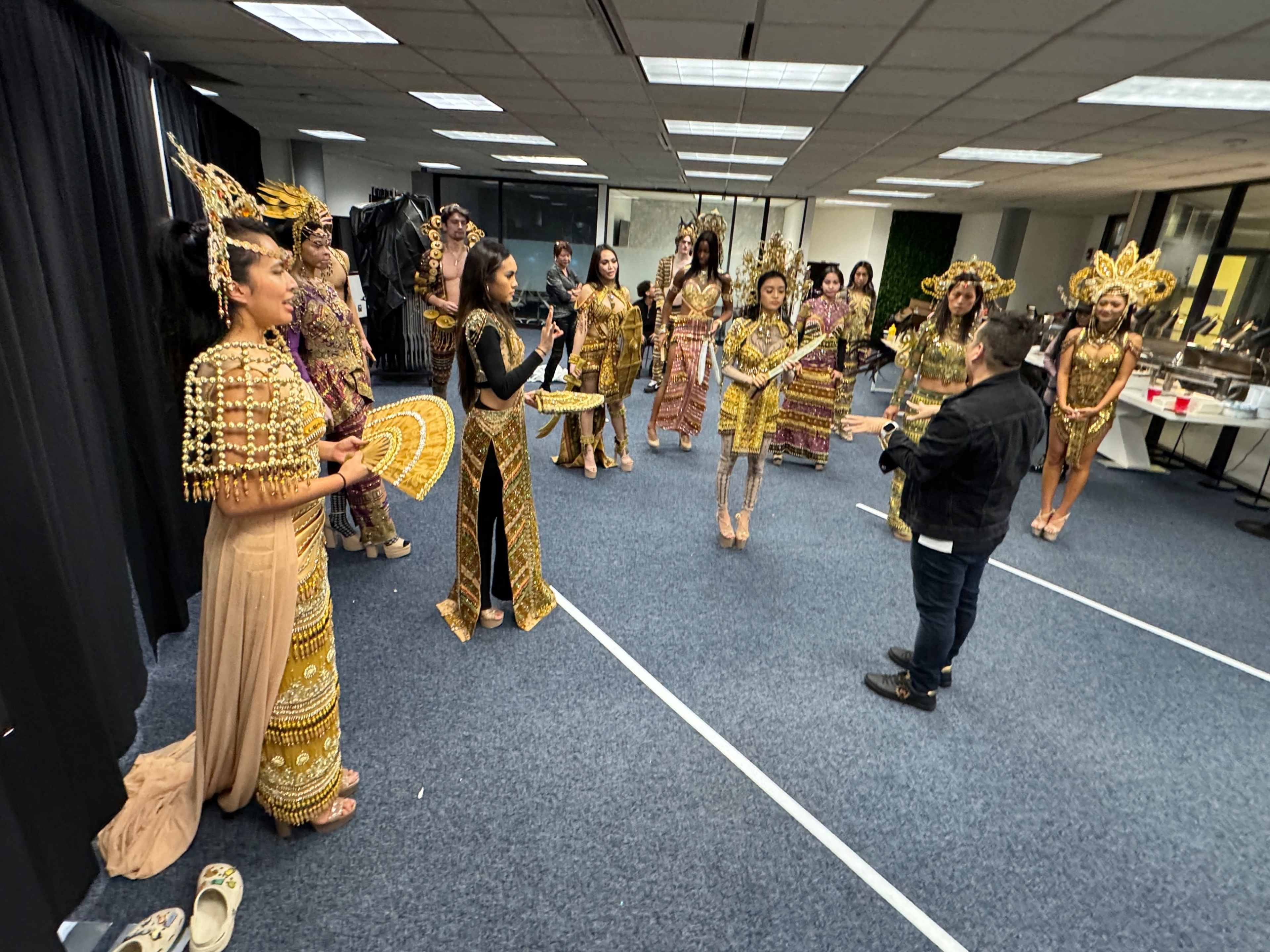 A group of individuals in elaborate traditional costumes are gathered in a spacious room, preparing for an event.