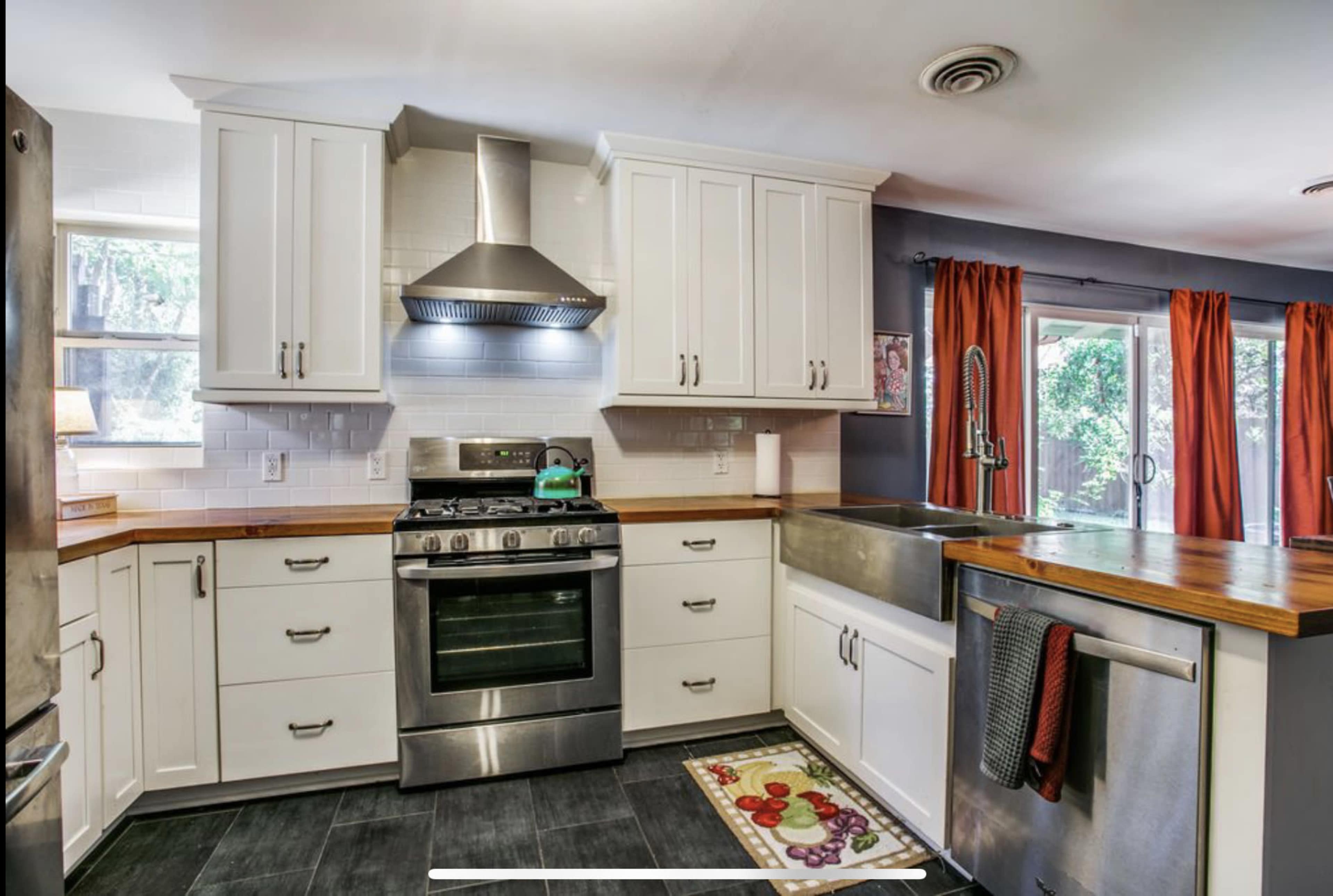 The kitchen features white cabinetry, a stainless steel stove and hood, and a large farmhouse sink with a wooden countertop.
