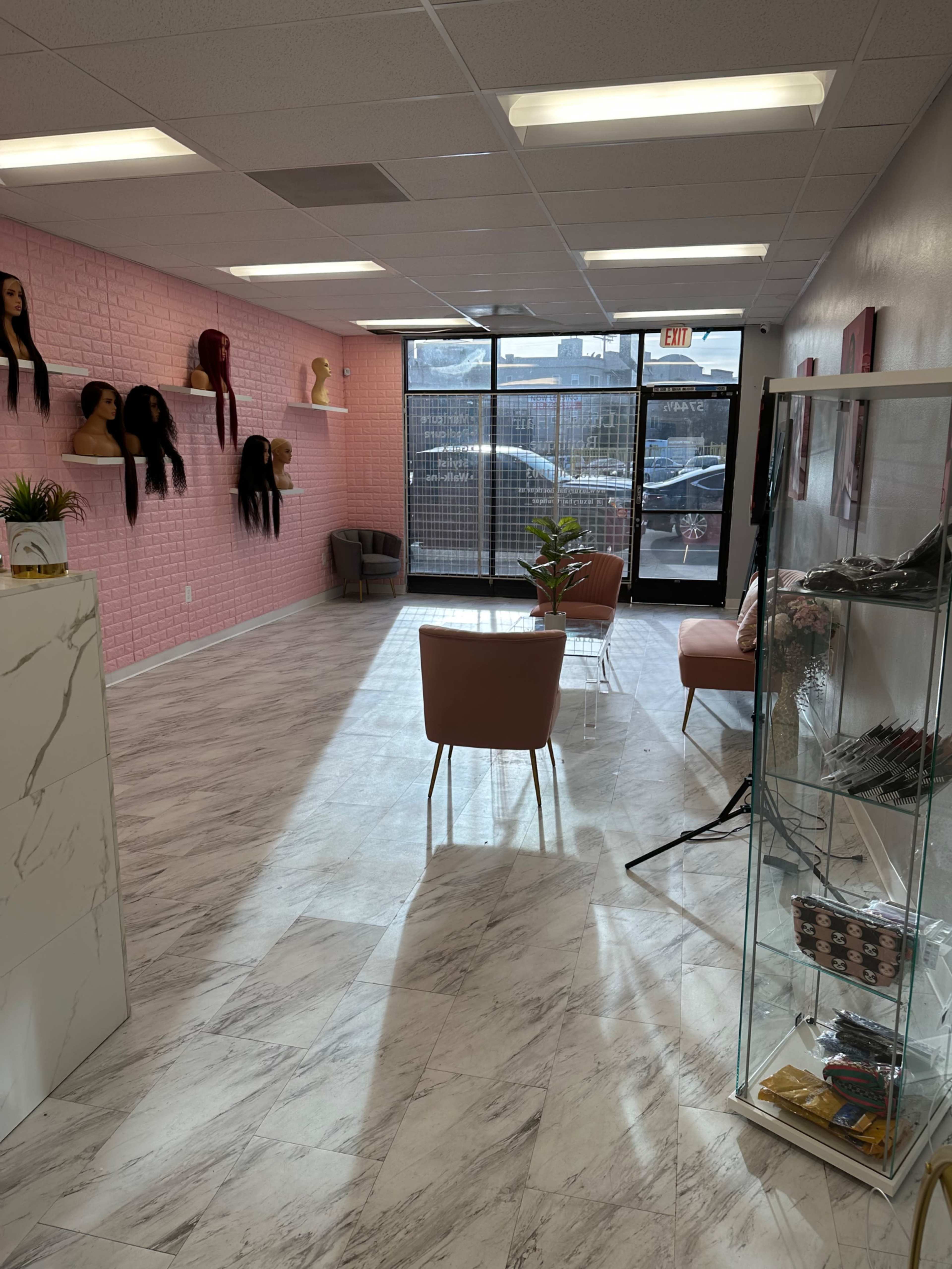 The interior of a hair salon features a pink brick wall adorned with mannequin heads, modern seating, and a display case filled with hair products.