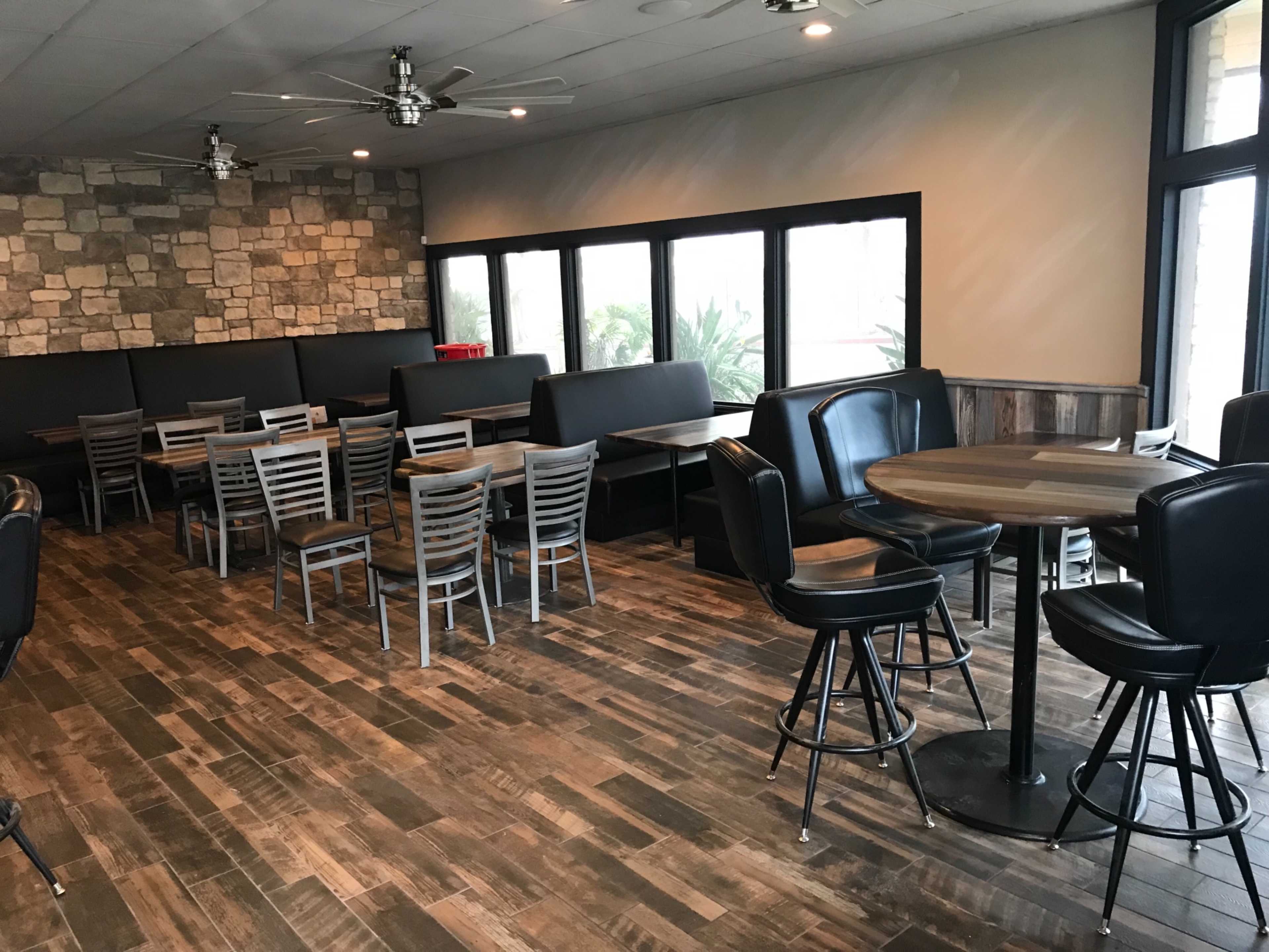 A cafe interior with wooden flooring, stone walls, and a mix of booth and table seating arranged around large windows.