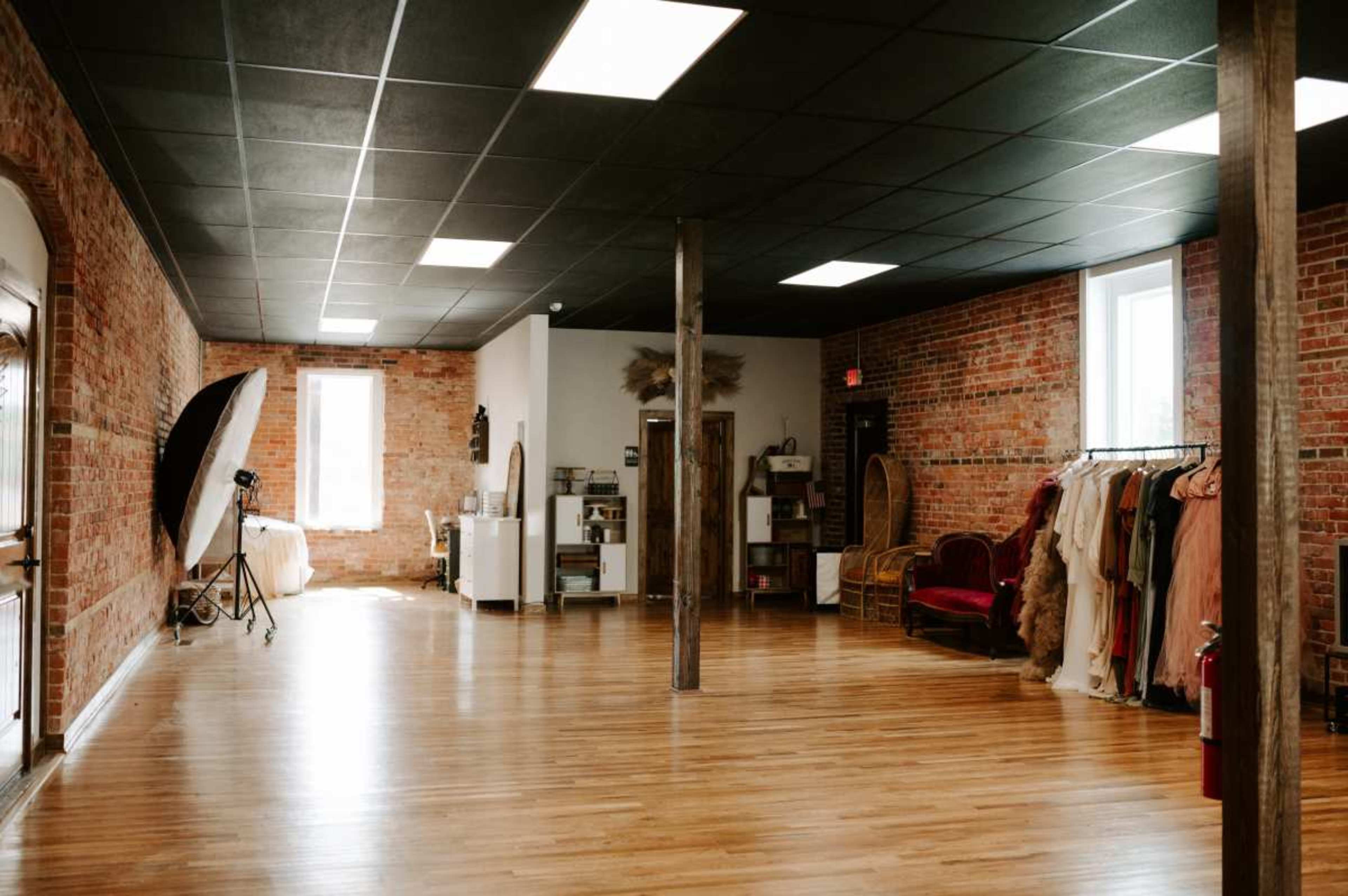 A spacious studio with wooden flooring, exposed brick walls, and racks of clothing, along with a photography setup in one corner.