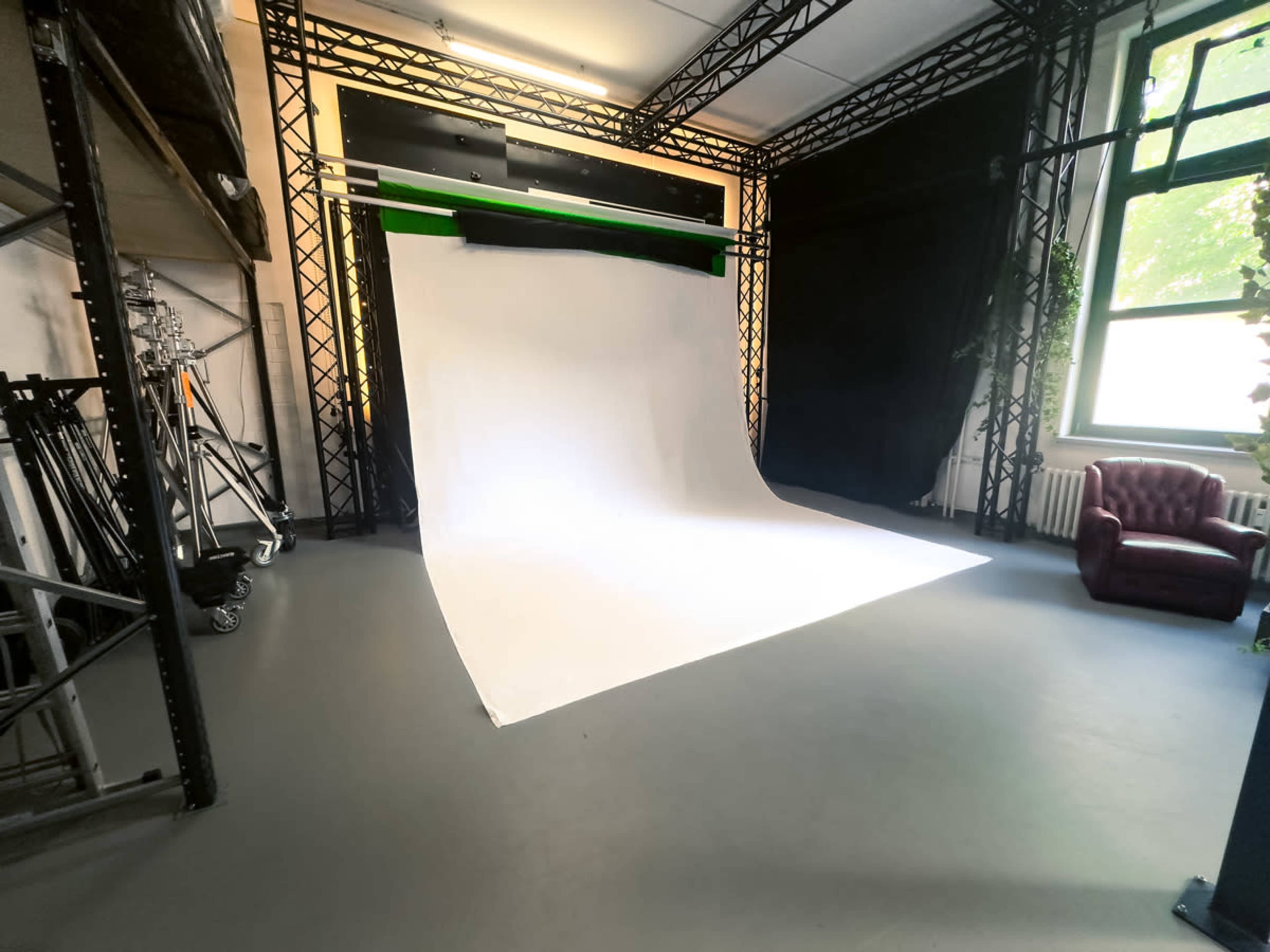 A photography studio with a white backdrop, a black draped area, and a maroon chair.