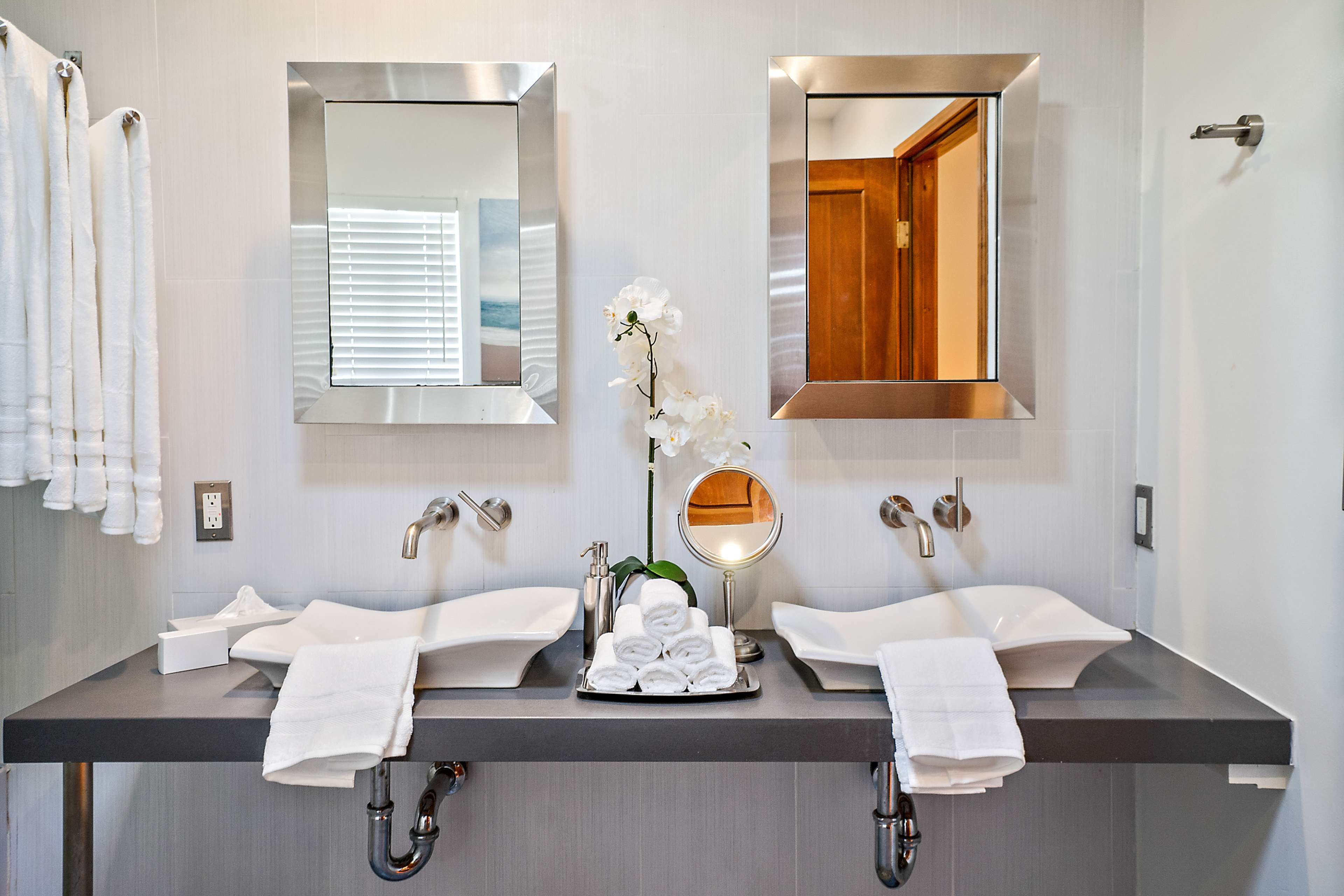 A modern bathroom features two sinks with minimalist design, framed mirrors above them, and neatly arranged towels and toiletries on the countertop.