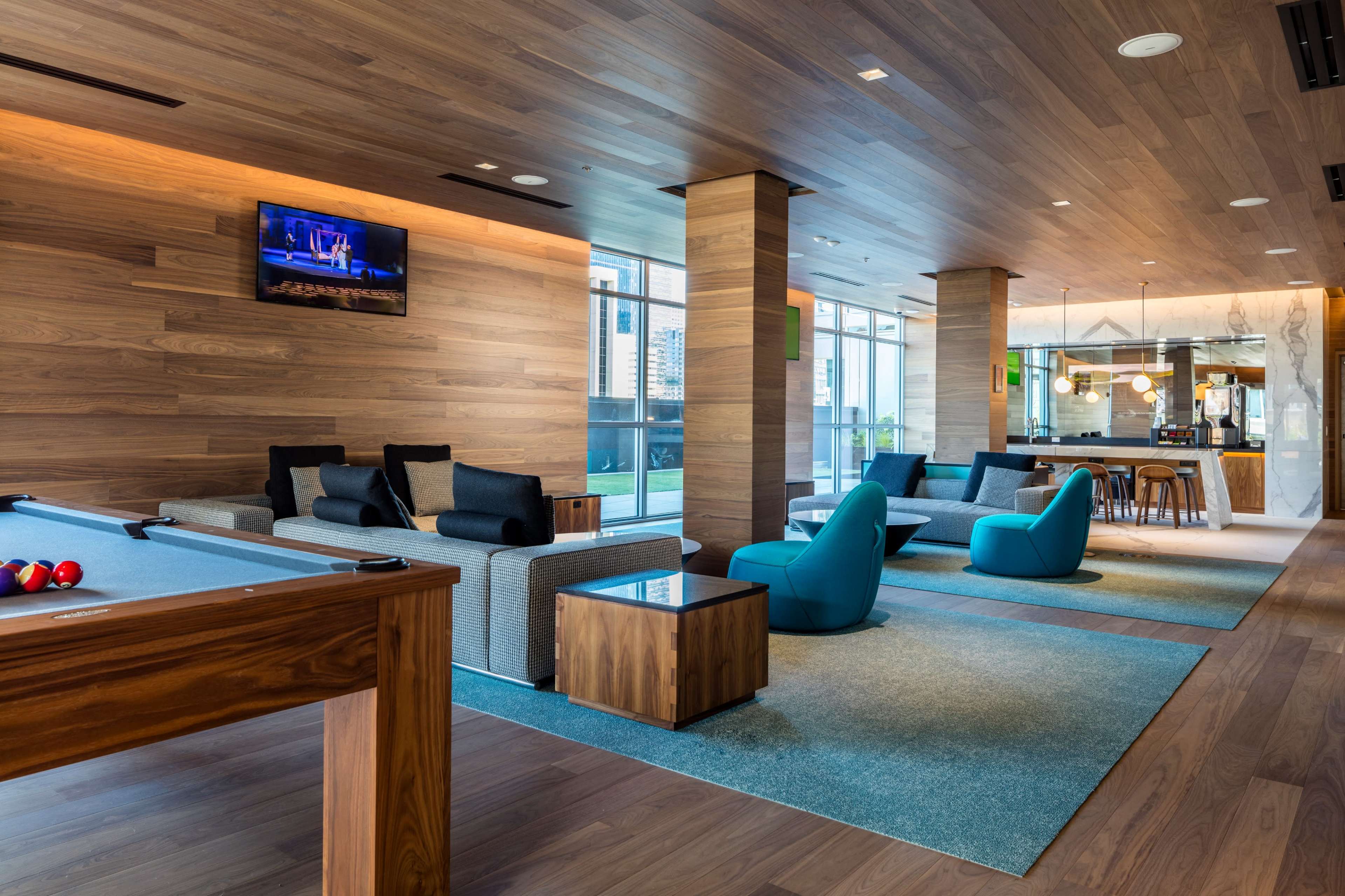A modern lounge area featuring a pool table, comfortable seating with blue cushions, and a bar in the background.
