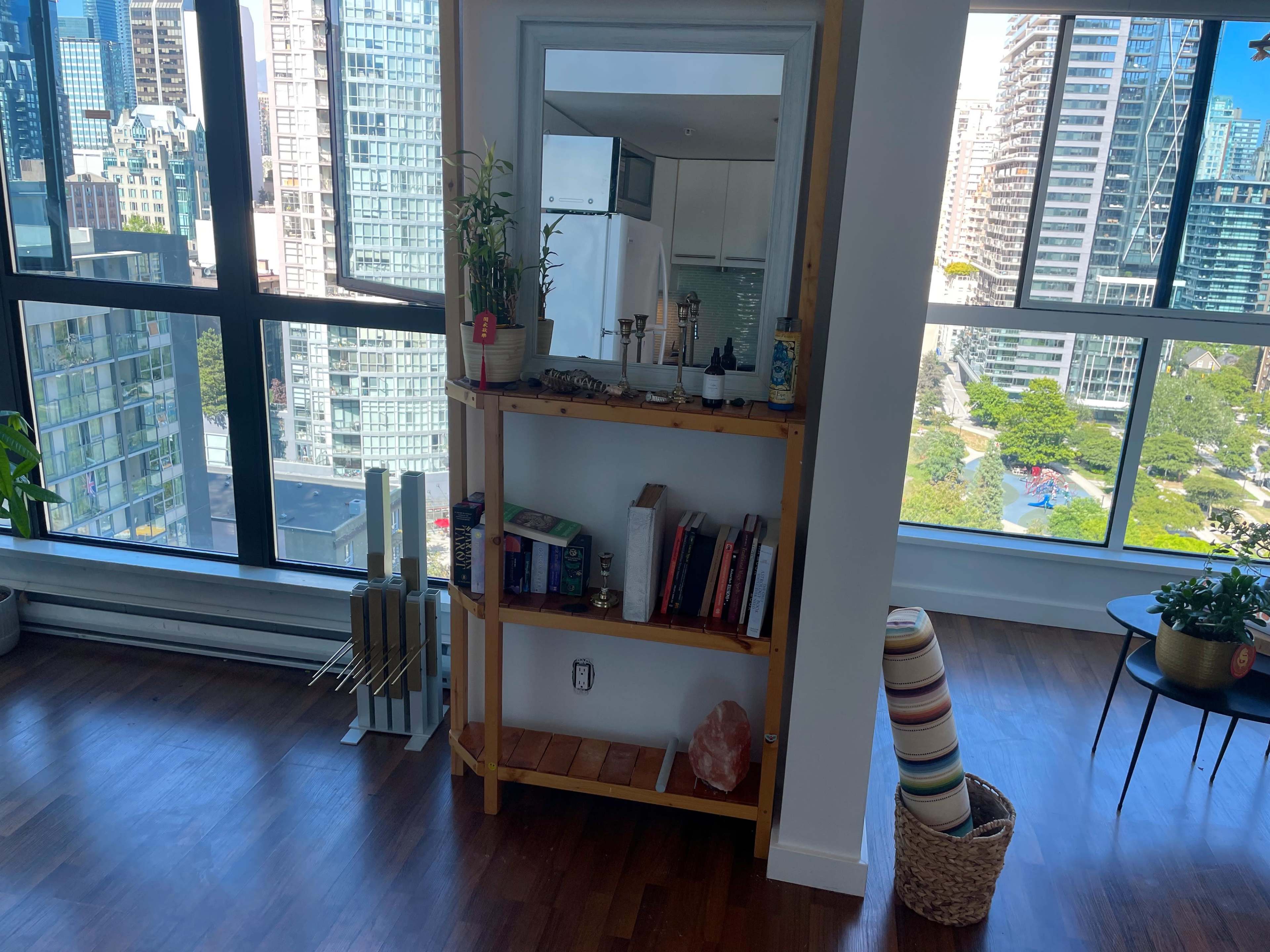 A bright, modern living space with a wooden shelf displaying books and decorative items beside large windows overlooking a cityscape.